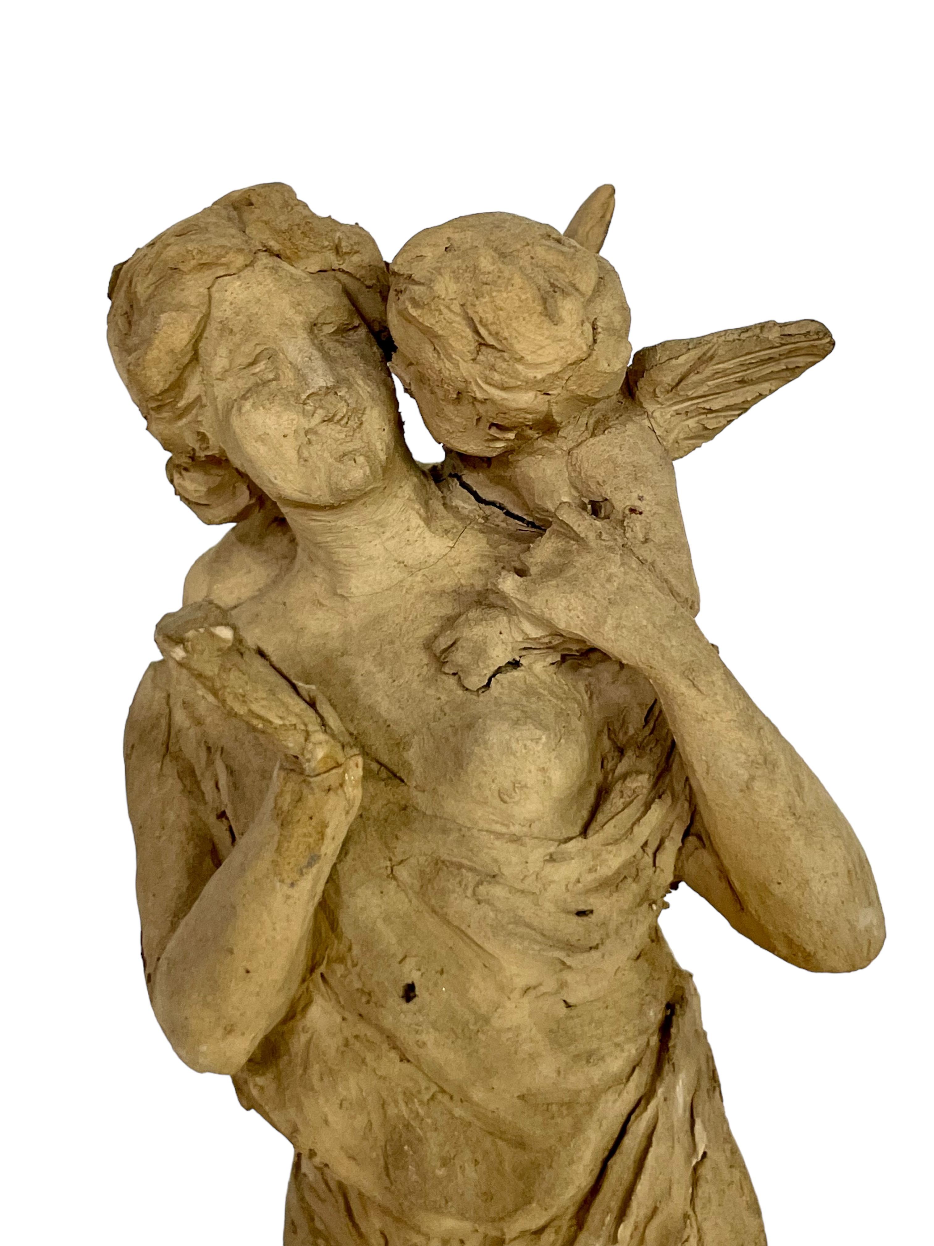 Una superba statuetta in terracotta che raffigura una donna in stile greco con un abito fluente, all'orecchio della quale un cherubino alato sta sussurrando. Anche se realizzato in stile rustico, i dettagli sono affascinanti, con un carattere