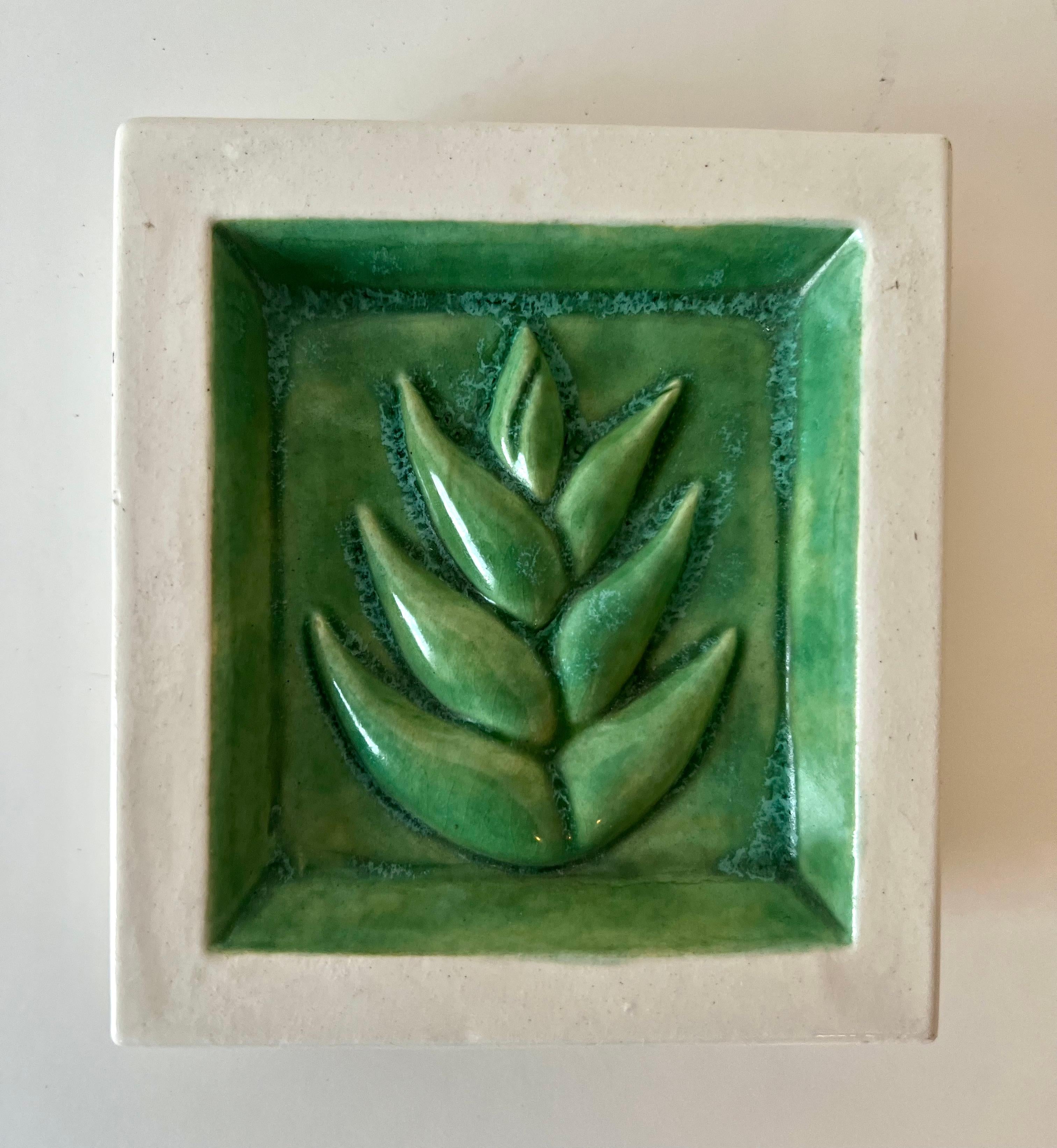 A small Terracotta Tile with a green leaf. The tile has enough relief to actually hold paper clips or small candies, but likely would be used for decorative purposes.