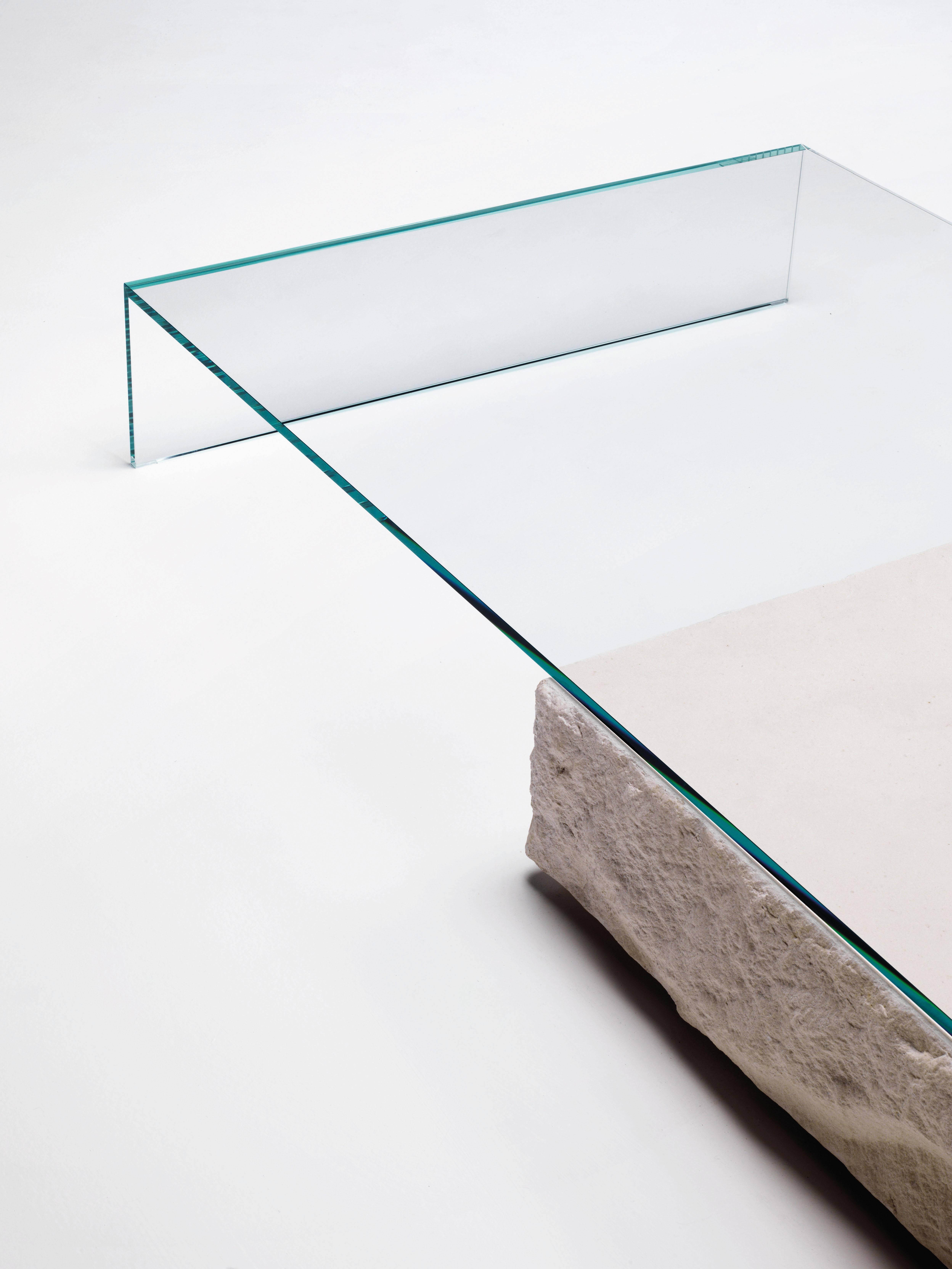 La table basse Terraliquida est présentée ici dans le verre extralight transparent. Table basse composée d'une pierre calcaire parallélépipédique d'aspect monolithique et d'un élément en verre extralight transparent à 45° collé et trempé de 15 mm