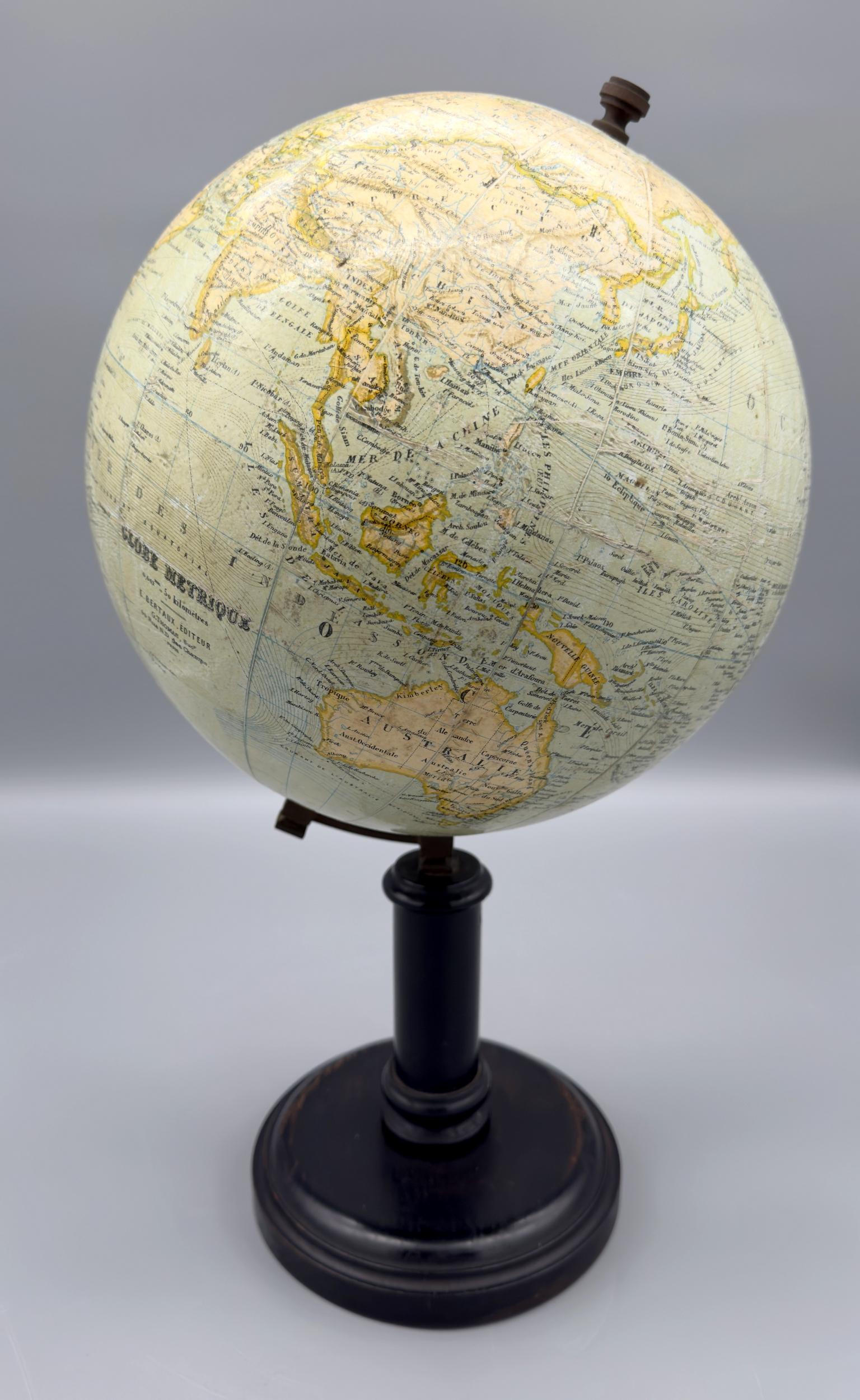 Pivoting physical globe, in polychrome printed paper mounted on plasterboard. The globe is attached by a brass clamp to a cylindrical base in blackened and waxed turned wood.
It’s inscribed “Globe métrique”, Editeur E. Bertaux, G. Thomas successeur