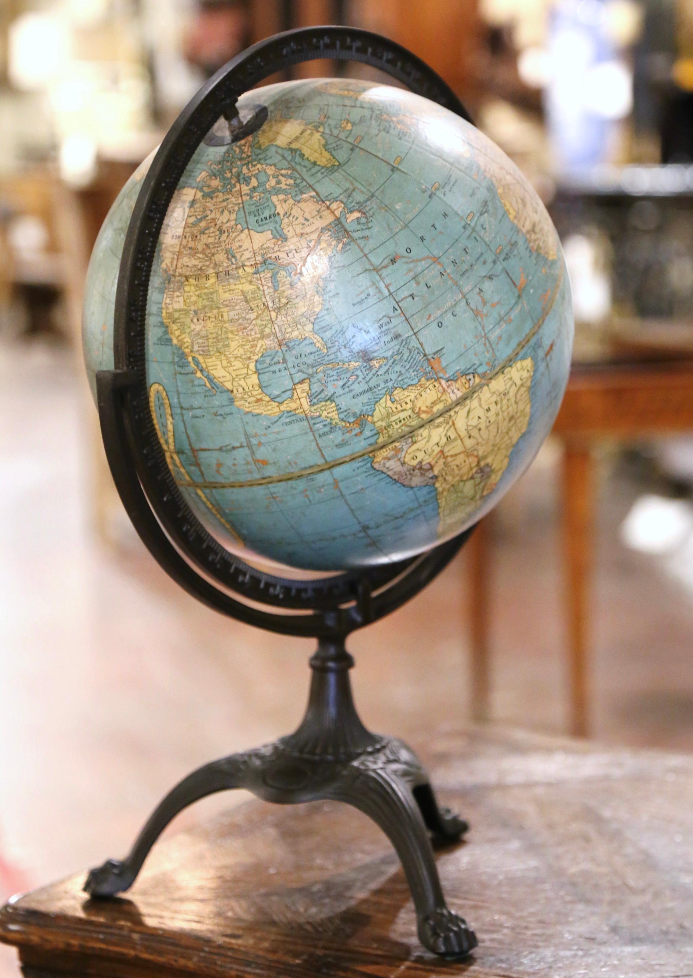 Decorate an office or a study with this elegant antique globe. Crafted in Indianapolis, Indiana circa 1946, the collectible piece sits on a bronze painted cast iron tripod base decorated with paw feet; it features a brass half meridian. The stem