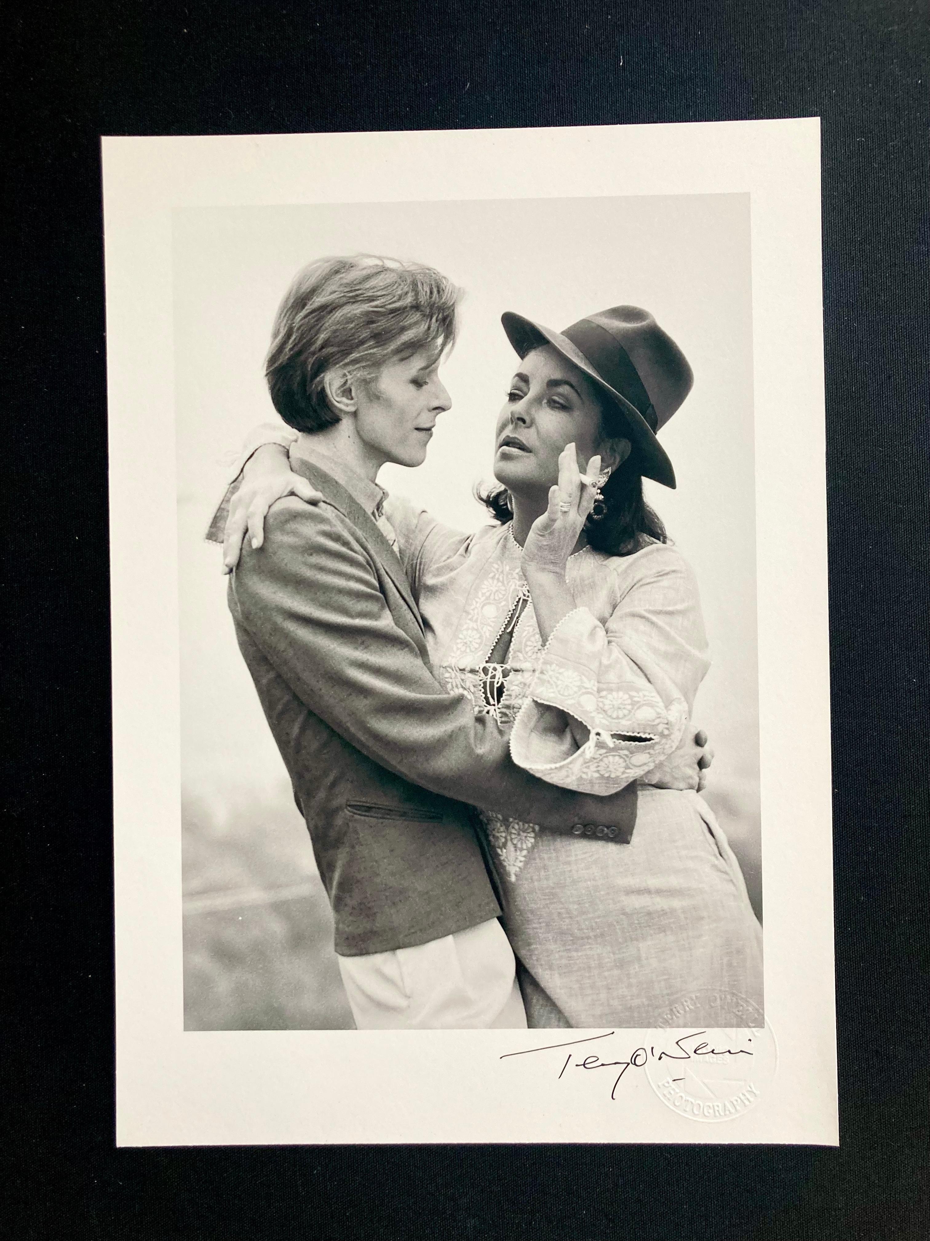 Signierter, 8" x 10" großer Archivdruck von David Bowie und Elizabeth Taylor in offener Auflage von Terry O'Neill, mit Terry O'Neills offiziellem, geprägtem Studiostempel.

David Bowie und die Schauspielerin Elizabeth Taylor treffen sich zum ersten