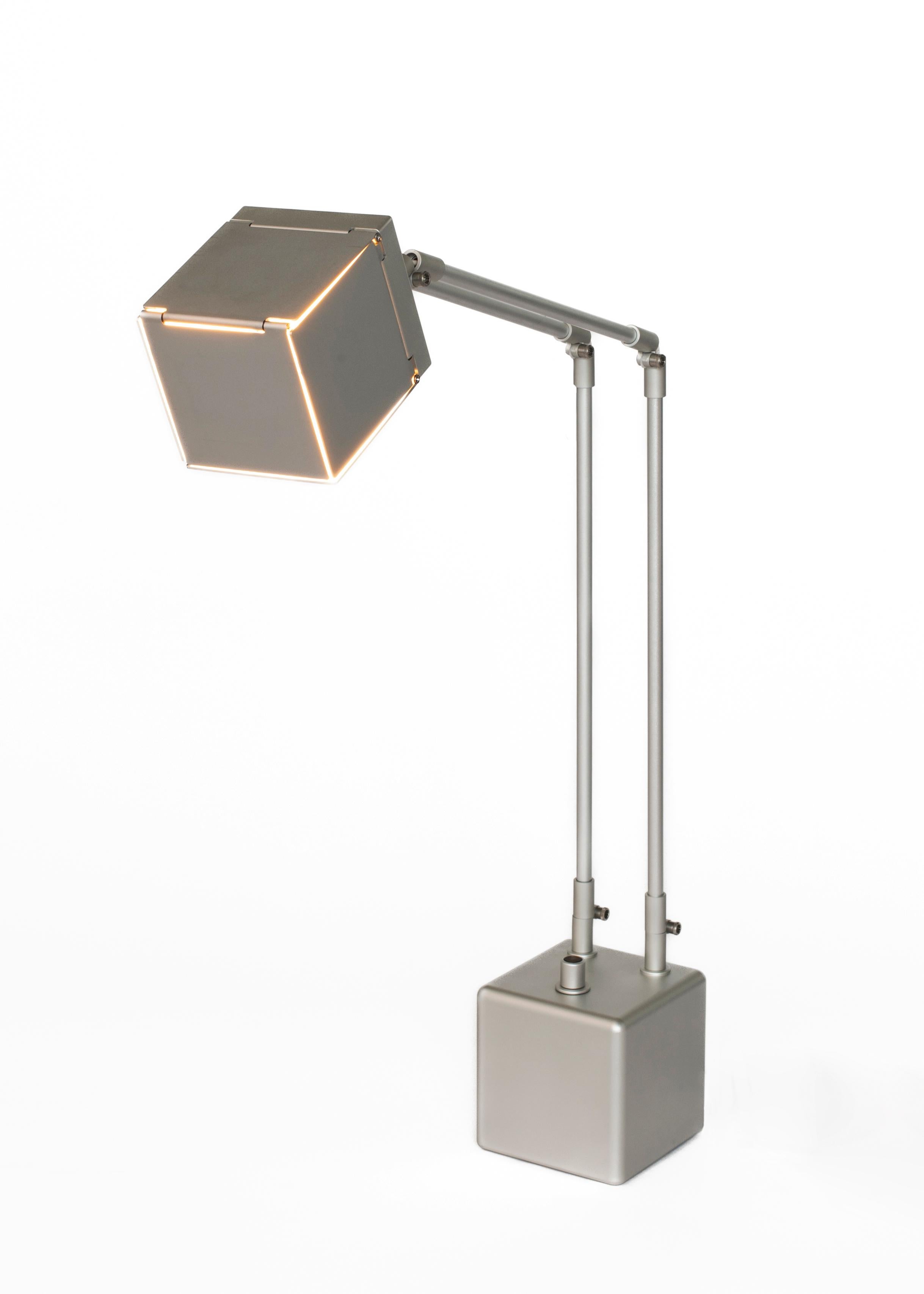 The Téssara Aktís Desk Lamp highlights the deceptive complexity of a cube. When folded and closed, its edges are illuminated. When opened, the light is revealed and reflects upon its interior mirror-polished faces. Through its various forms, it