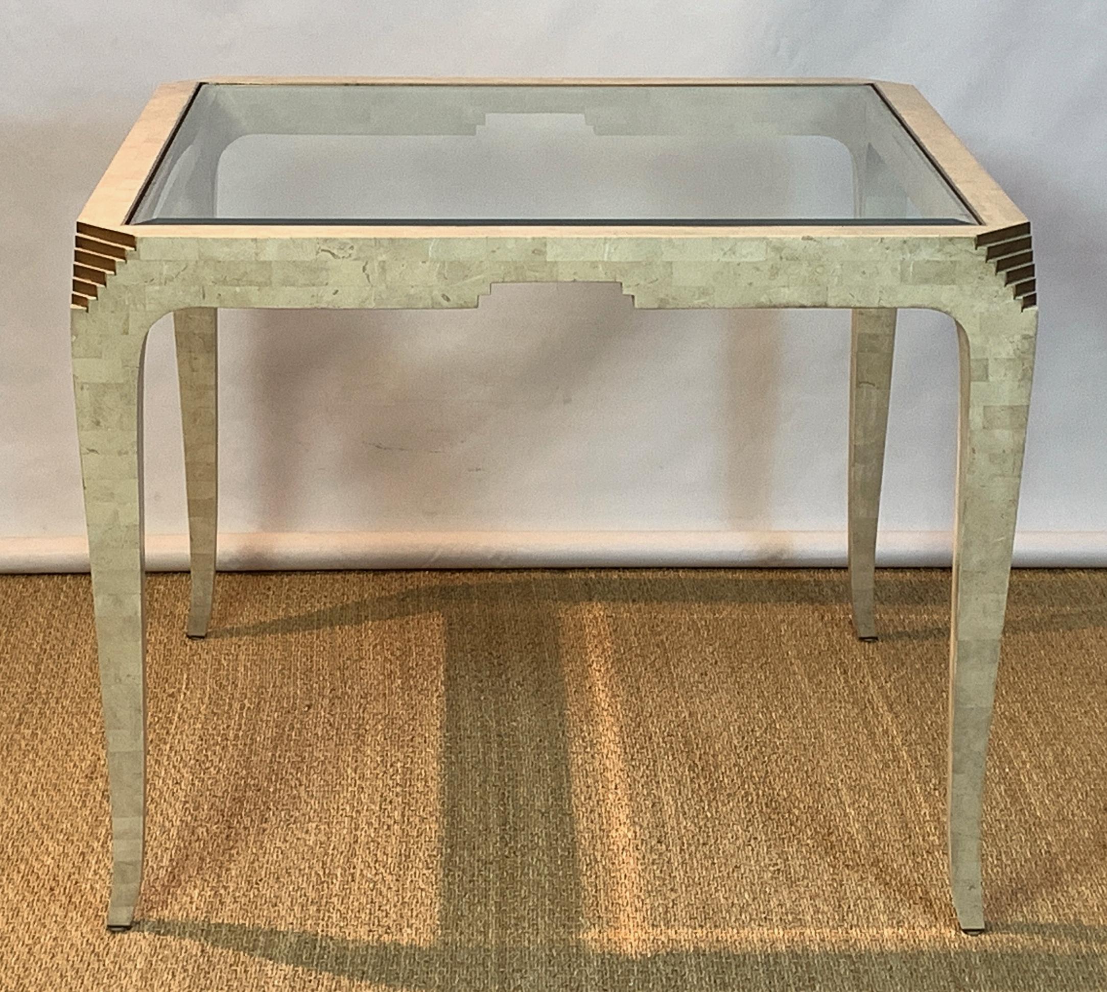 A fantastic mid-20th century tessellated coral stone games table with brass trim. The Art Deco Revival table was designed by Merle Edelman for Casa Bique and features thin tapering legs with stepped brass accents to the canted corners and brass