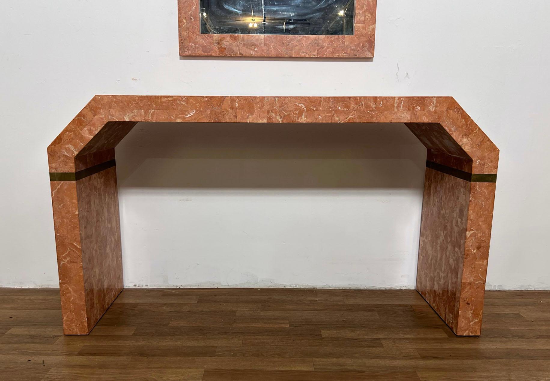 A postmodern mirror and console in coral toned tessellated fossil stone with brass trim, unmarked, but most likely by Maitland Smith.

The console measures 52