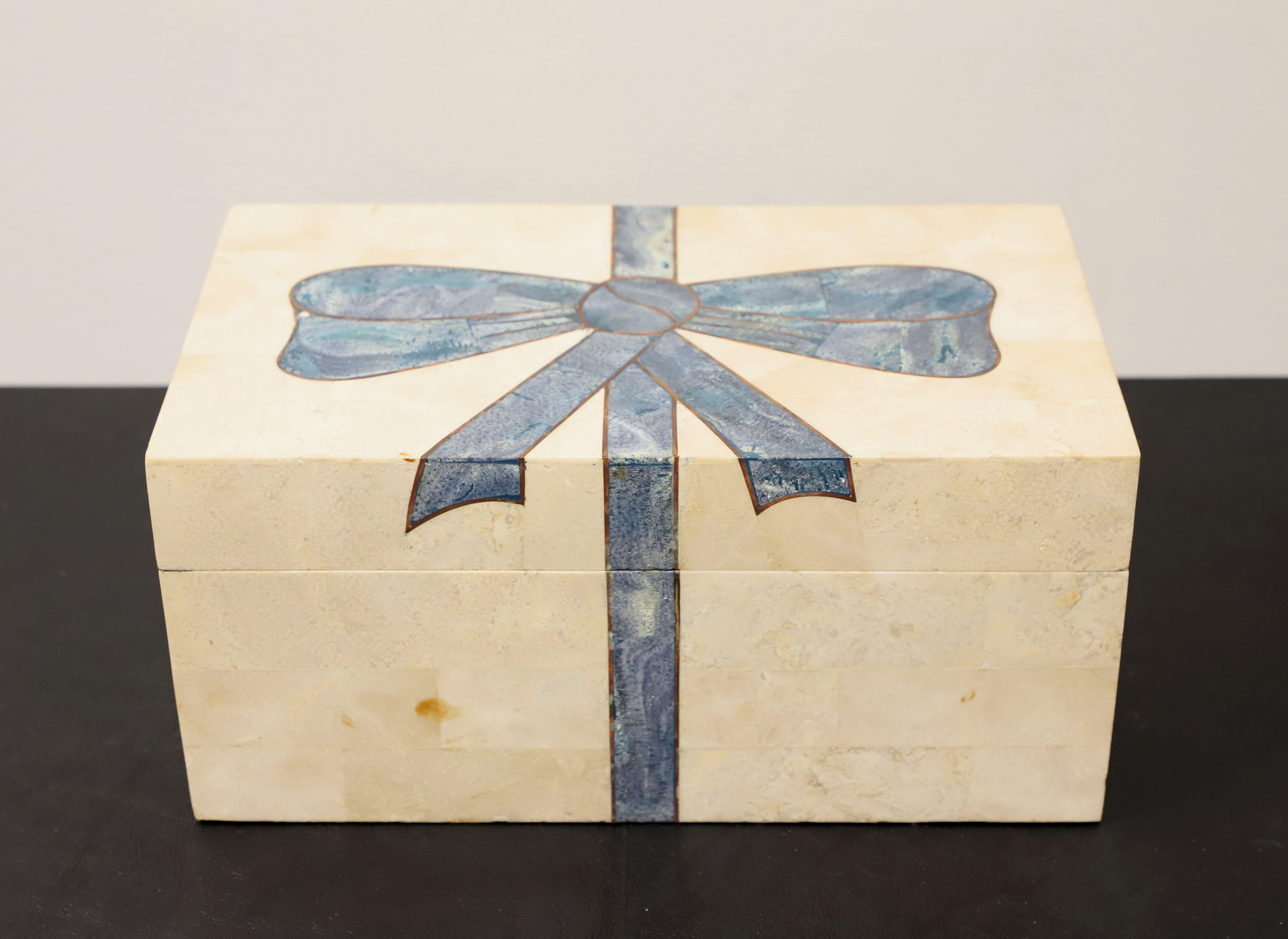 A trinket box in tessellated marble, possibly by Maitland Smith, though unmarked. Cream colored marble tiles with blue marble tiles forming a decorative bow in the center, ample black felt lined interior, brass hinge hardware, fabric strap held lid,