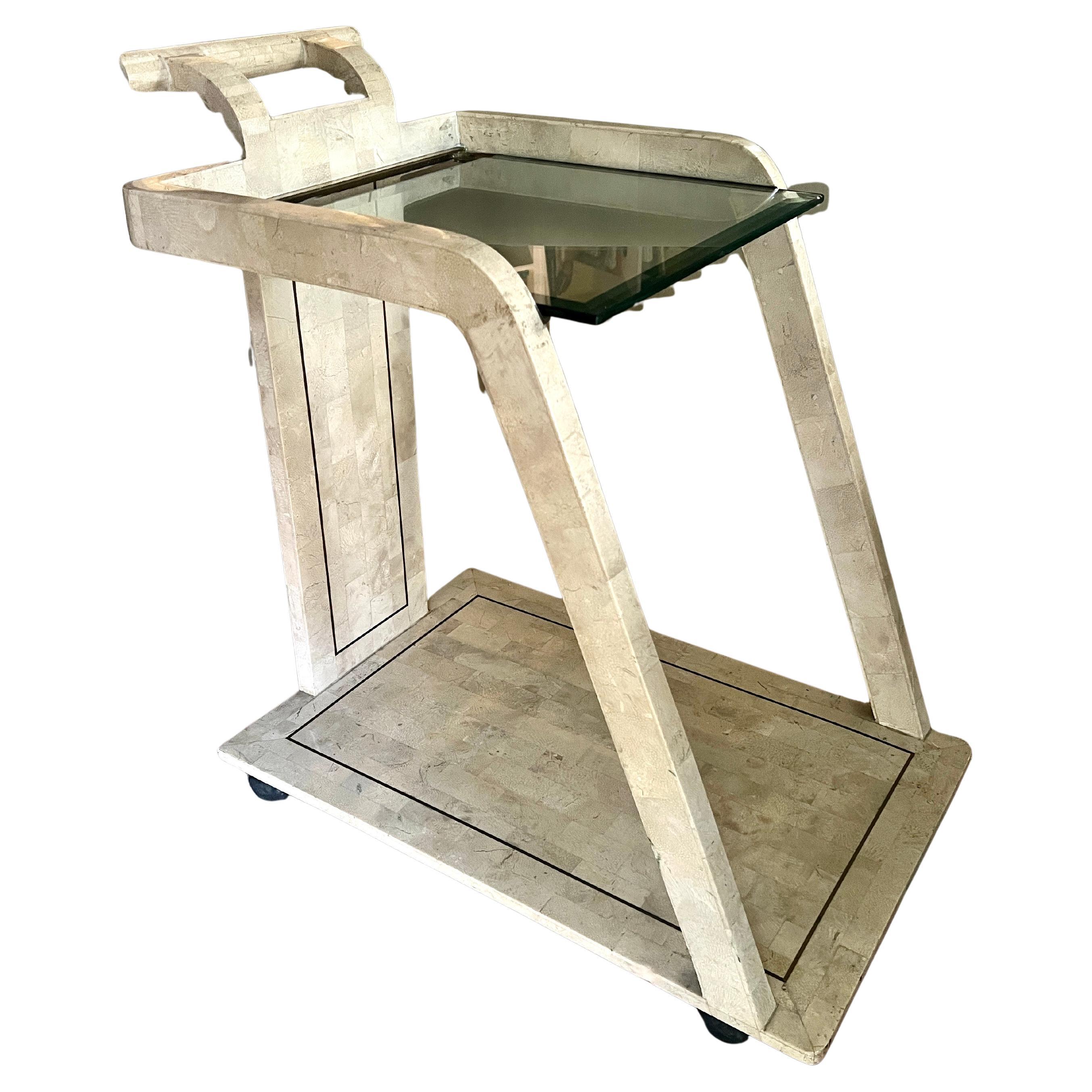 A very sleek and modern two tier bar cart - the piece is made of tessellated stone with an inlay banding of brass.  The top is glass that sits on a brass closure.  The shape is very unique and sexy - large handle and proportions make this piece a