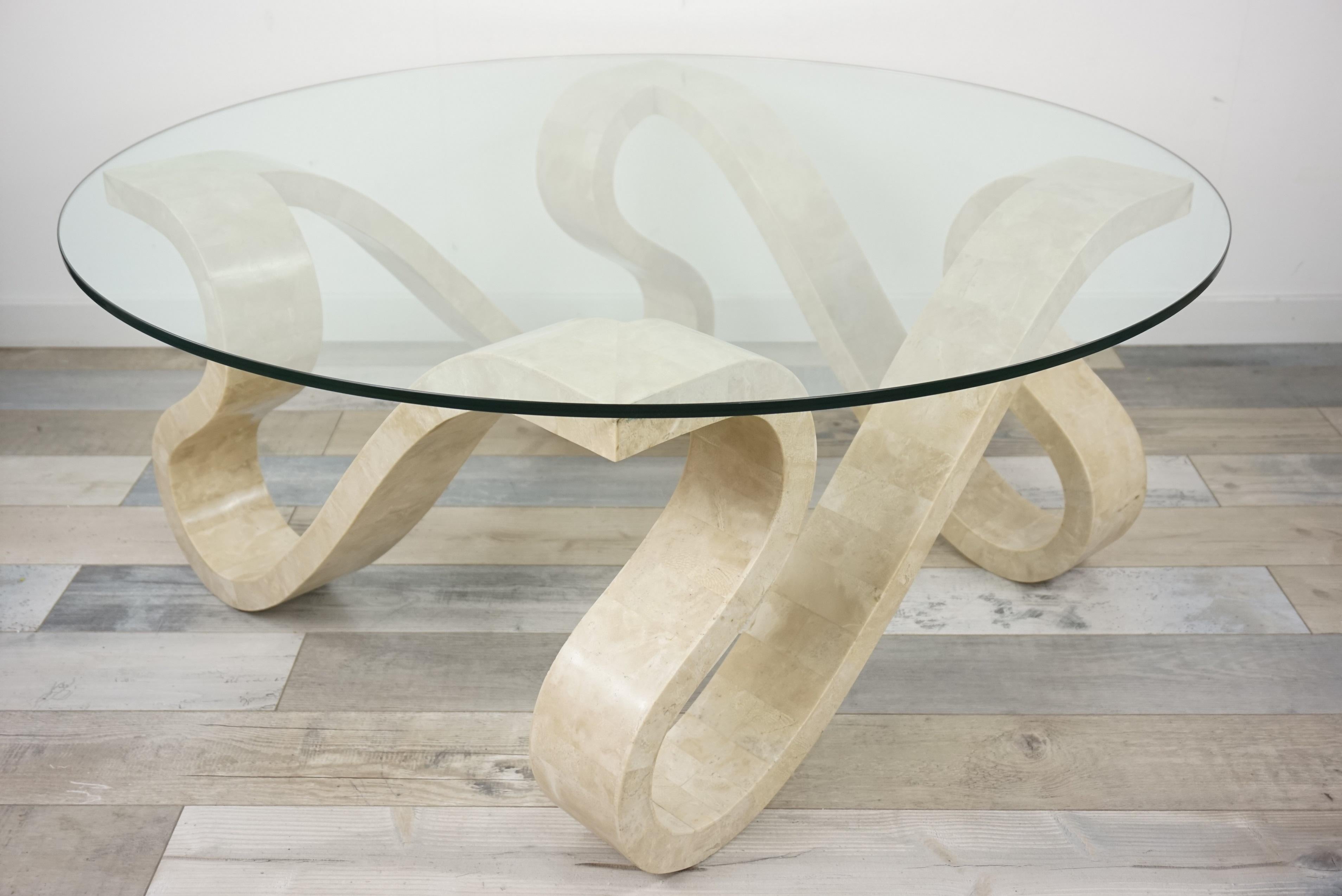 Hollywood Regency style coffee table with stone marquetry, generously shaped, welcoming and subtle work, finely made: the entire structure of the table is dressed with travertine pieces marquetry base with round glass tray. Hollywood Regency style,