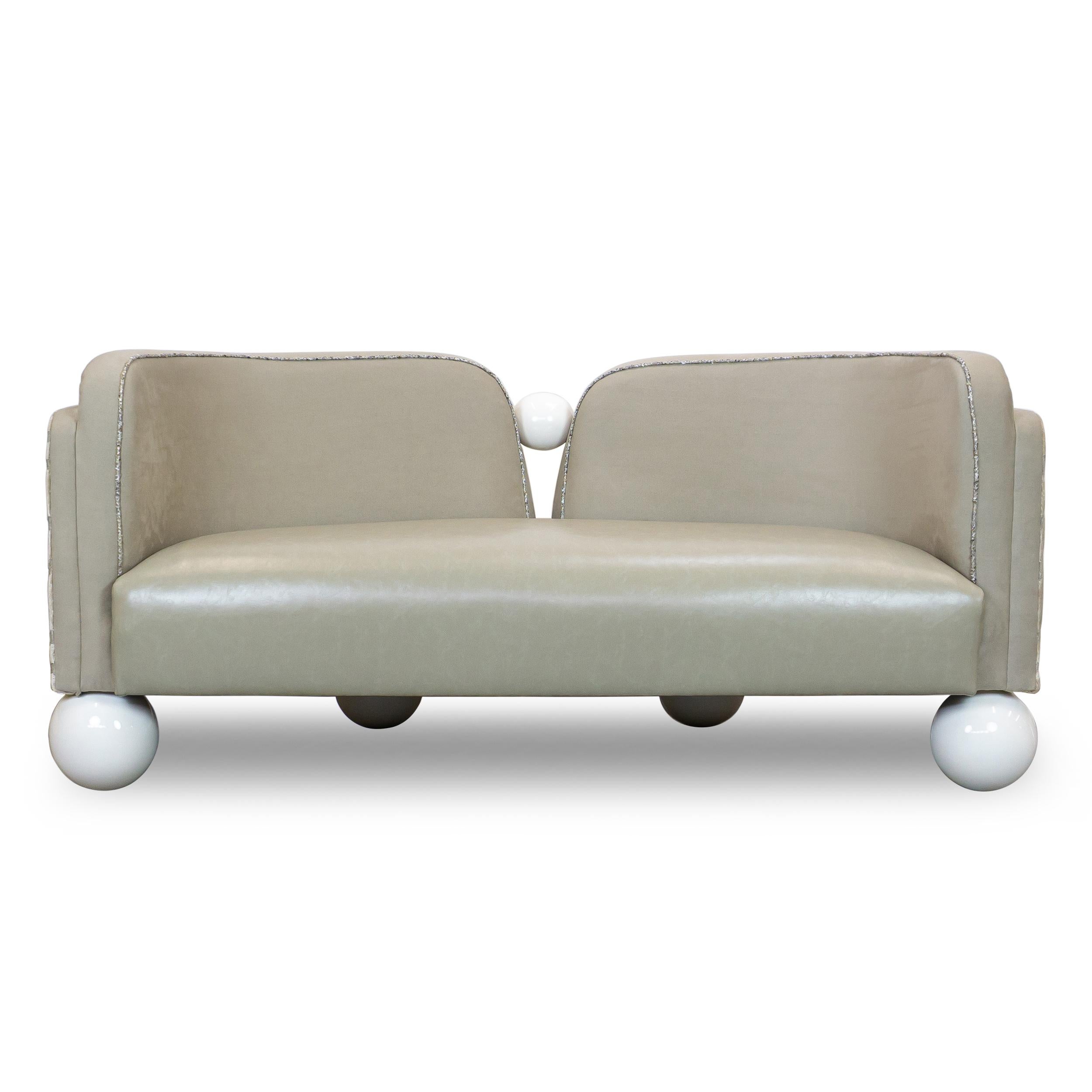 Sofá estilo tete a tete, de inspiración art-decó, con patas esféricas y elementos decorativos que parecen perlas. Tapizada en una combinación beige tonal de piel sintética y lana de corte neozelandés con estampado tribal. Construido con arce duro