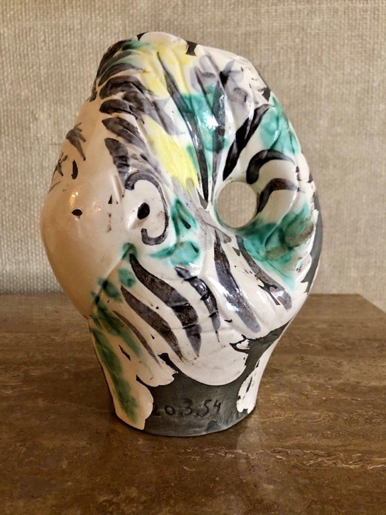 La Tête de Femme Couronnée de Fleurs (R. 237) di Pablo Picasso, realizzata nel 1954, incarna la sua padronanza della ceramica come mezzo di narrazione e astrazione. Quest'opera dipinta a mano presenta una testa femminile coronata e ornata di fiori,