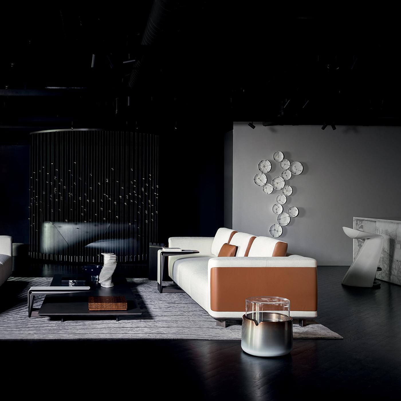 The TETI side table features a clear glass top paired with a light blue-copper lacquered base. Its design is characterized by a unique detail inspired by the uvula of Maserati cars, combining functionality with elegant lines to create a versatile