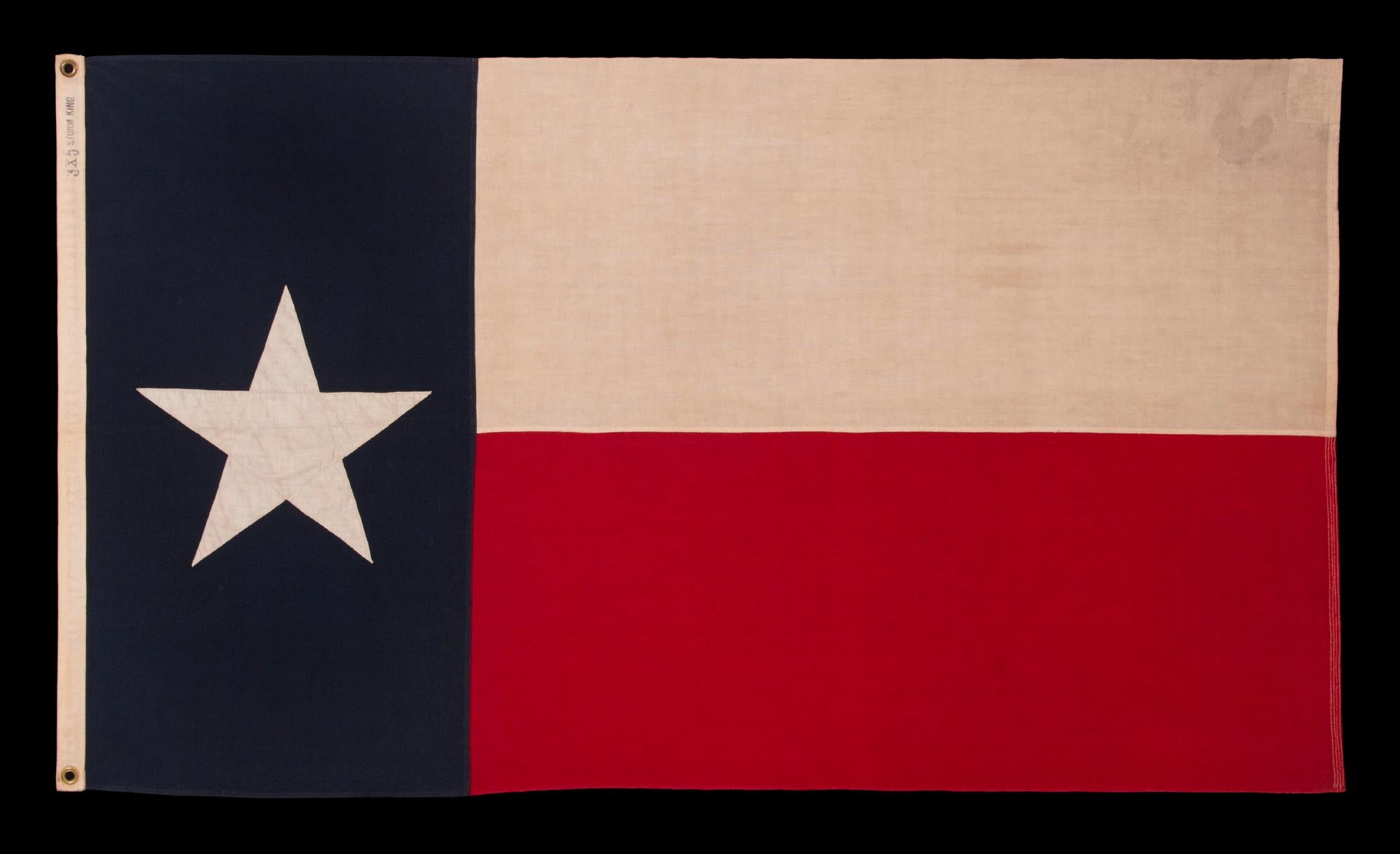 Texas state flag, made sometime in the period between the latter 1940’s and the 1950’s. The single star is made of cotton and is double-appliquéd (applied to both sides) with a zigzag machine stitch. The vertical bar and the two horizontal bars are