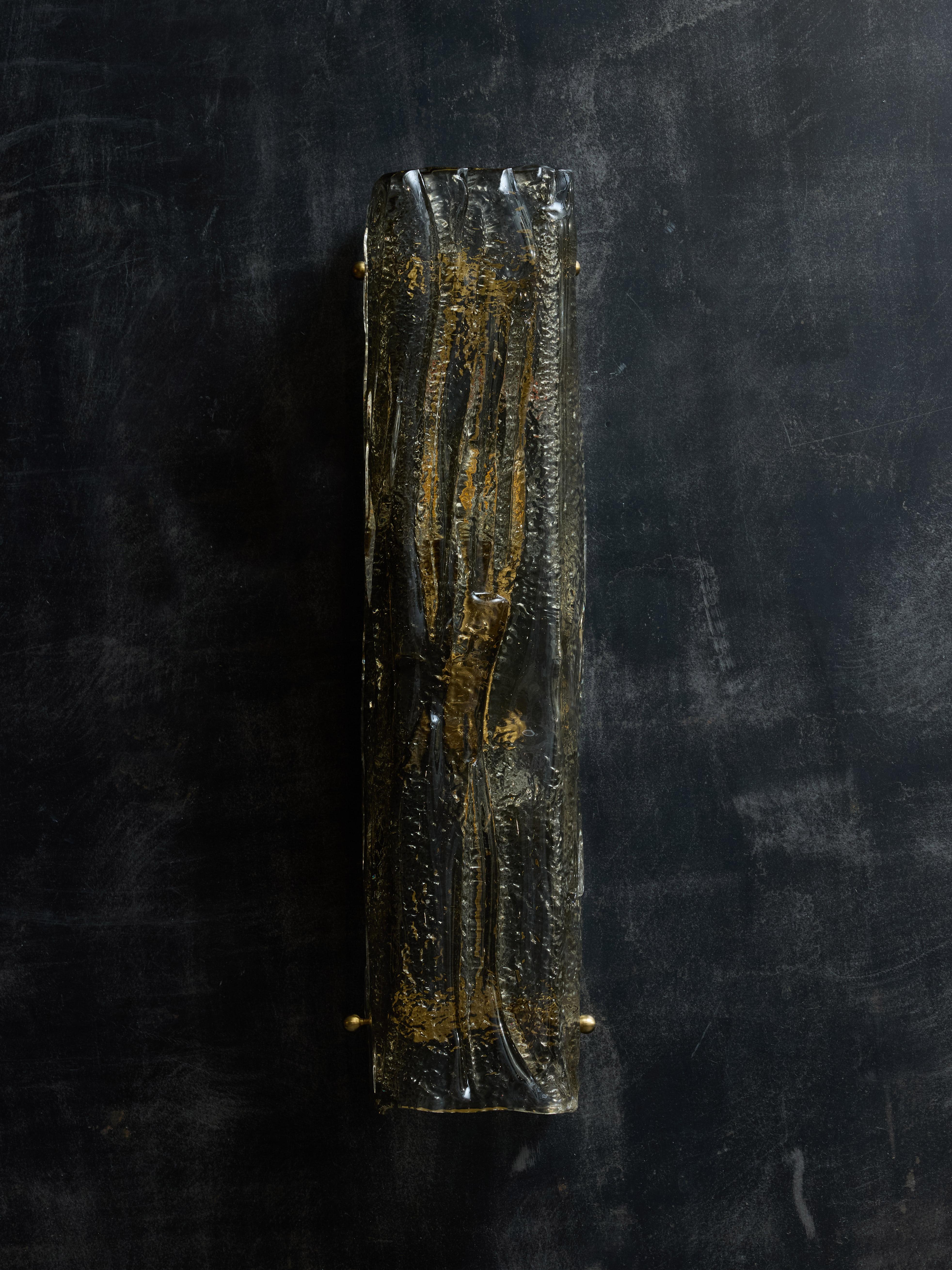 Applique realizzate con un unico pezzo di vetro di Murano piegato a forma di quadrato, leggermente ambrato e con motivi su tutta la superficie per diffondere la luce delle due fonti interne.