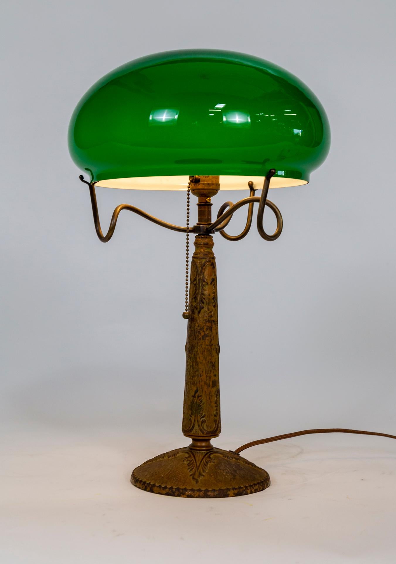 An Art Nouveau table lamp with a detailed, cast metal base and a unique, brass glass holder in the form of three curling stems. The green glass shade is a mushroom cap shape. One medium bulb socket with a beaded pull chain, newly wired. 1920s. Lamp