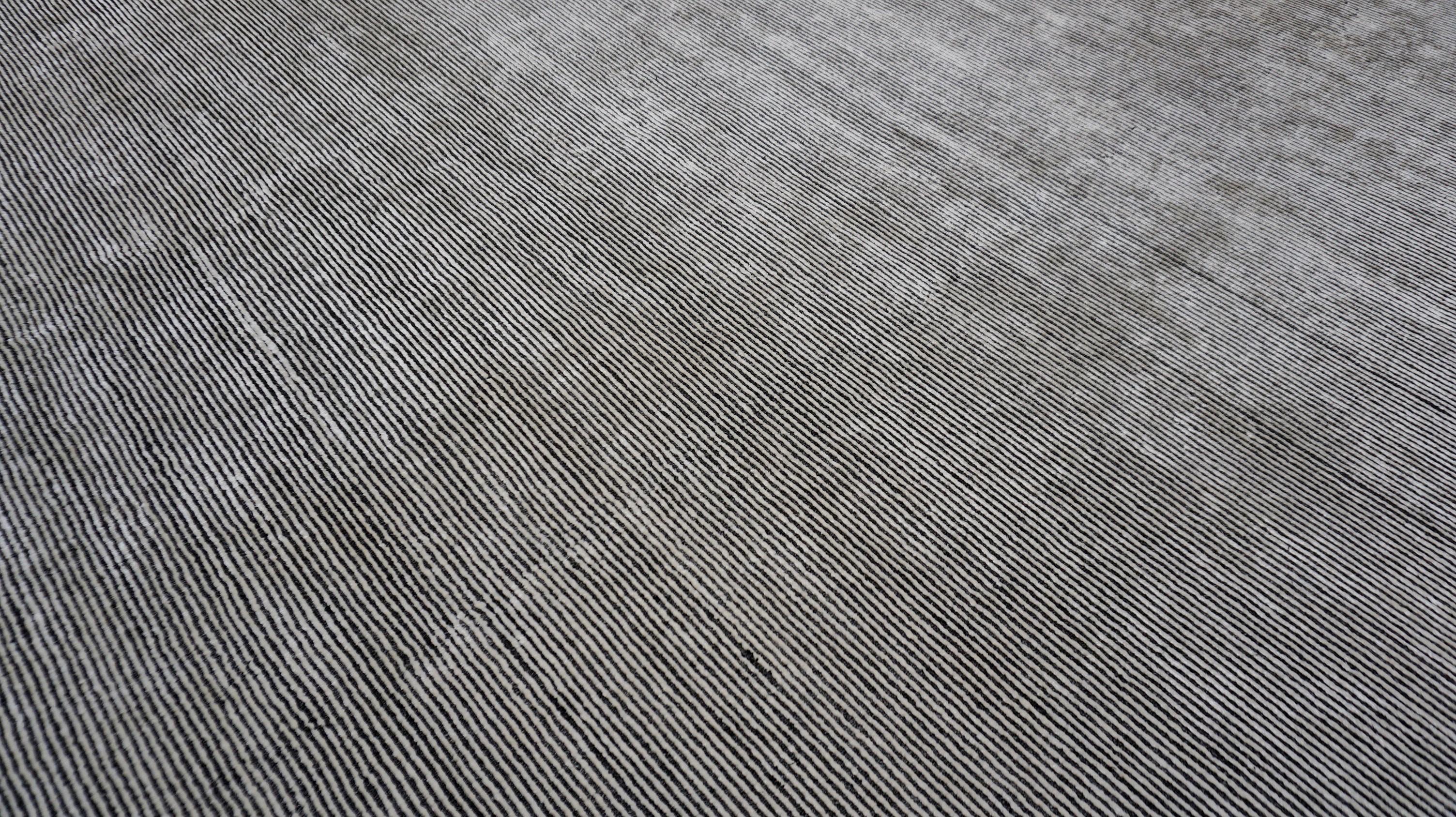 This hand-knotted wool blend rug embodies modern elegance with its subtle linear texture and refined charcoal gray, white, and ivory monochrome palette. The minimalist design features a delicate horizontal striation, creating a sense of depth and