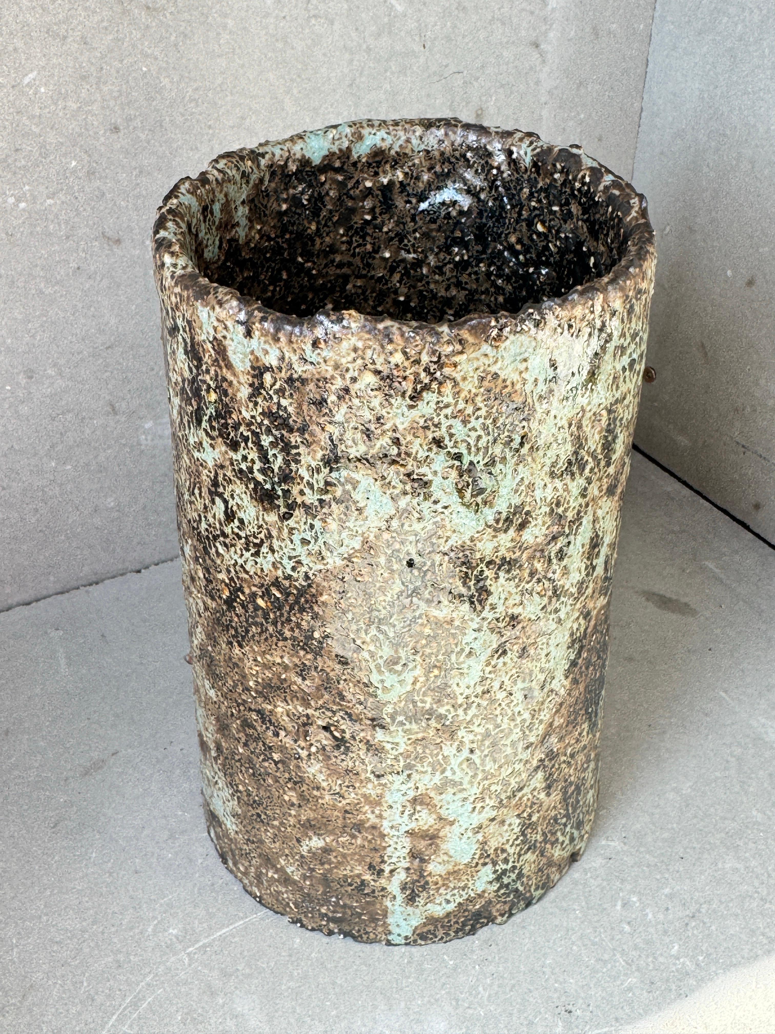 Questo vaso scultoreo in ceramica è un tranquillo monumento al decadimento e al rinnovamento naturale. La sua forma alta e cilindrica è avvolta da una superficie profondamente strutturata, stratificata con smalti simili alla cenere che ricordano la