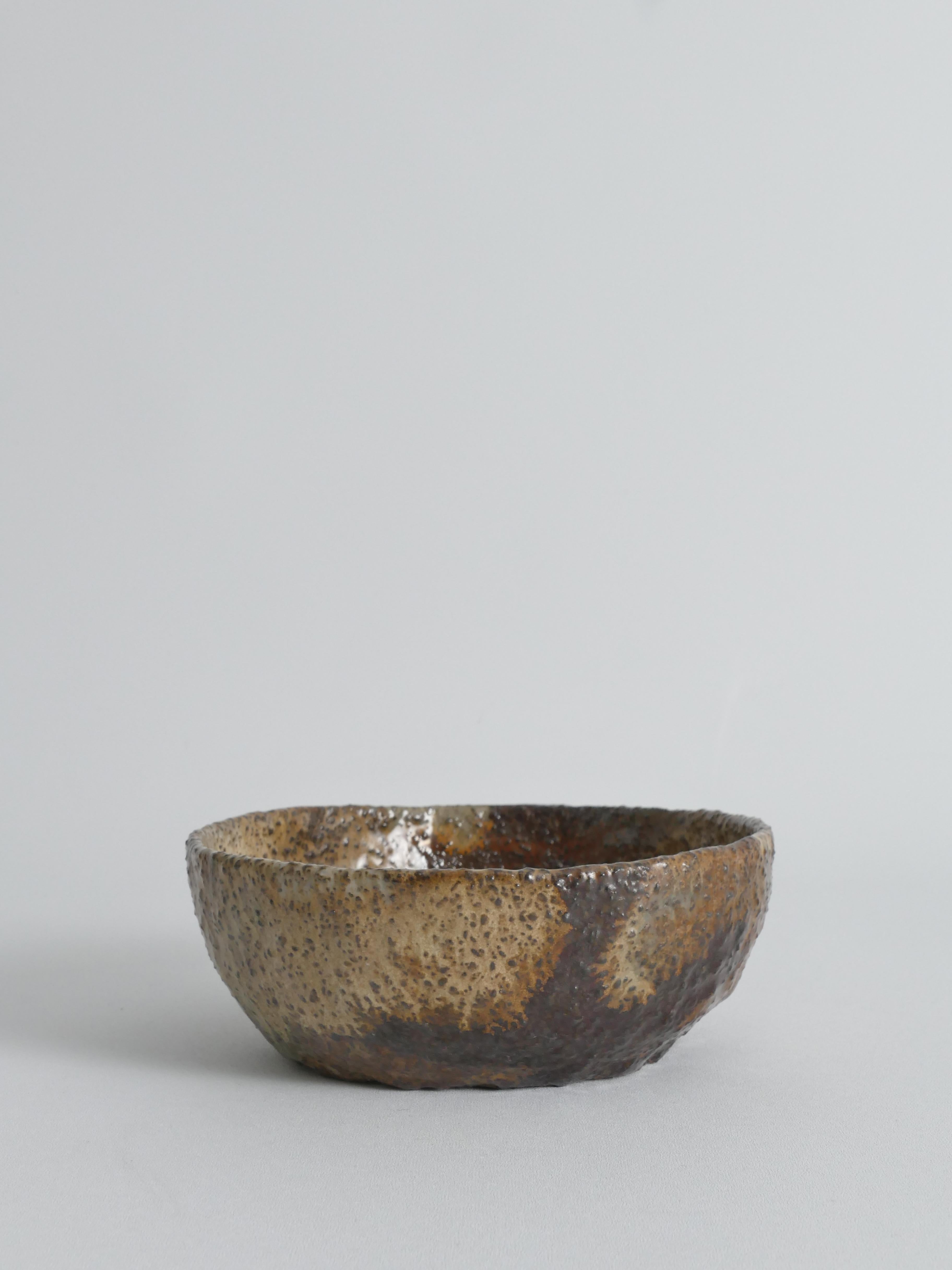 This striking handmade stoneware bowl exemplifies the organic beauty of mid-century studio pottery. Formed by hand, it features a rustic, tactile surface with a rich interplay of earthy glazes in mottled brown, moss green, and amber tones, accented