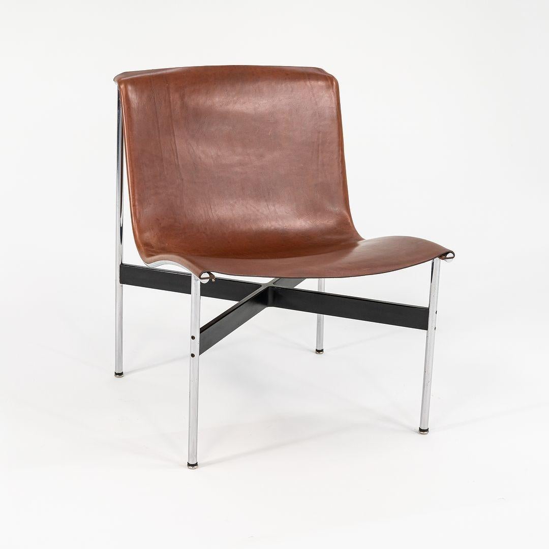 This is a TG-12 sling lounge chair in tan leather with a polished chrome frame and black t-bar, produced by Gratz Industries. The chair was designed in the 1950s by Katavolos, Littell and Kelley, distributed by Erwine and Estelle Laverne's
