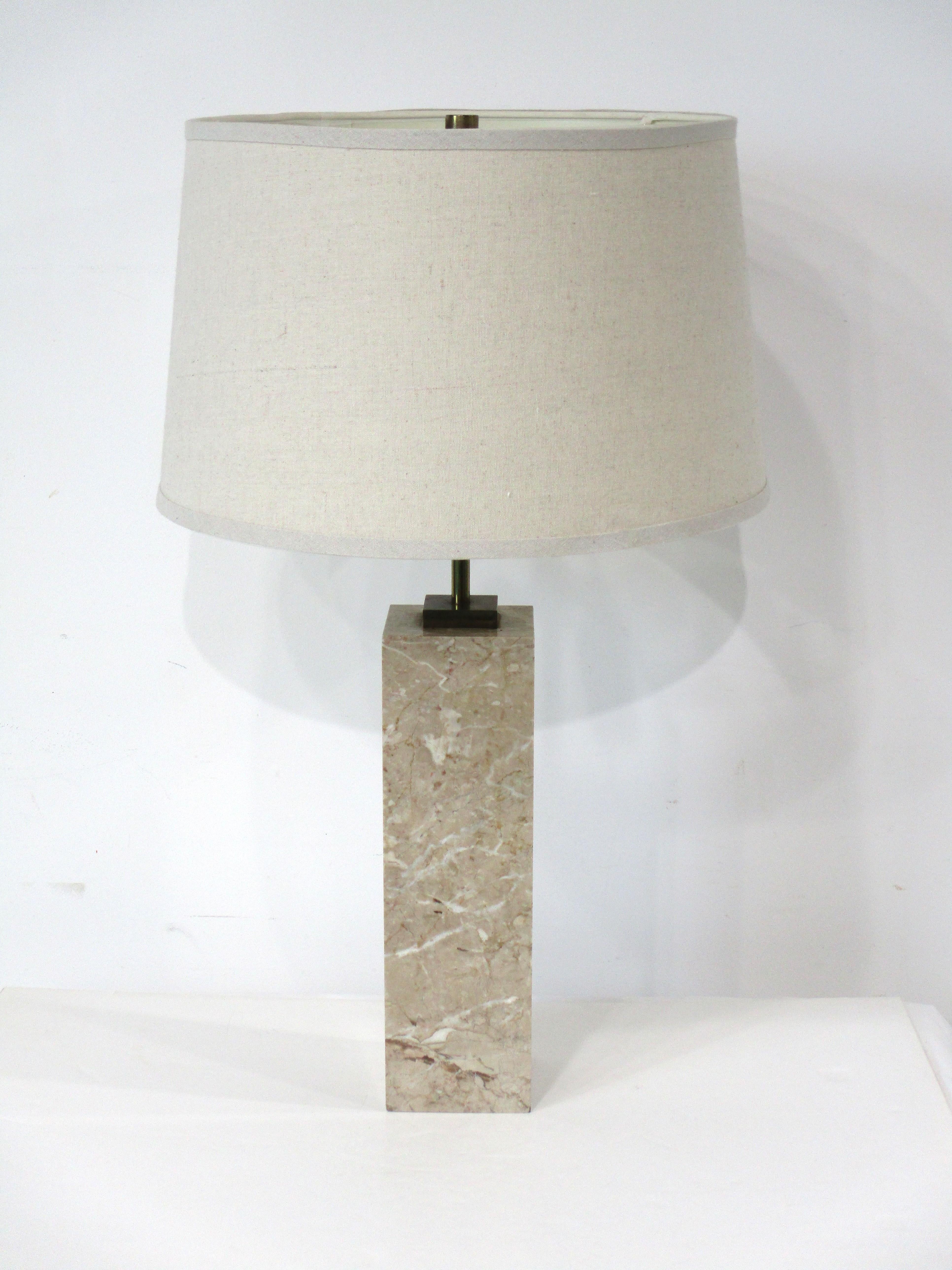 A squared marble based table lamp with great veining having brass upper detail and double sockets and pull chain switch . Topped with a woven lighter beige barrel shade giving the piece a tailored and tight look . Designed by T.H. Robs John -