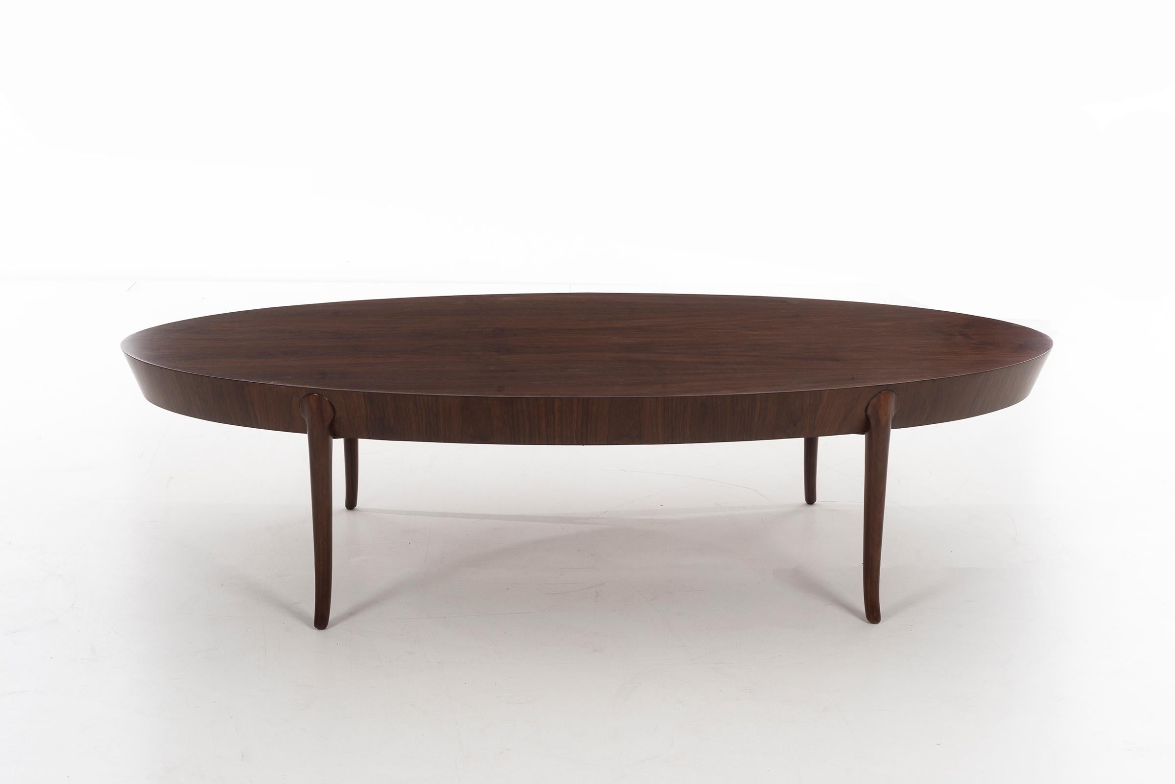 Walnut veneer oval cocktail table with beveled edge and saber legs.