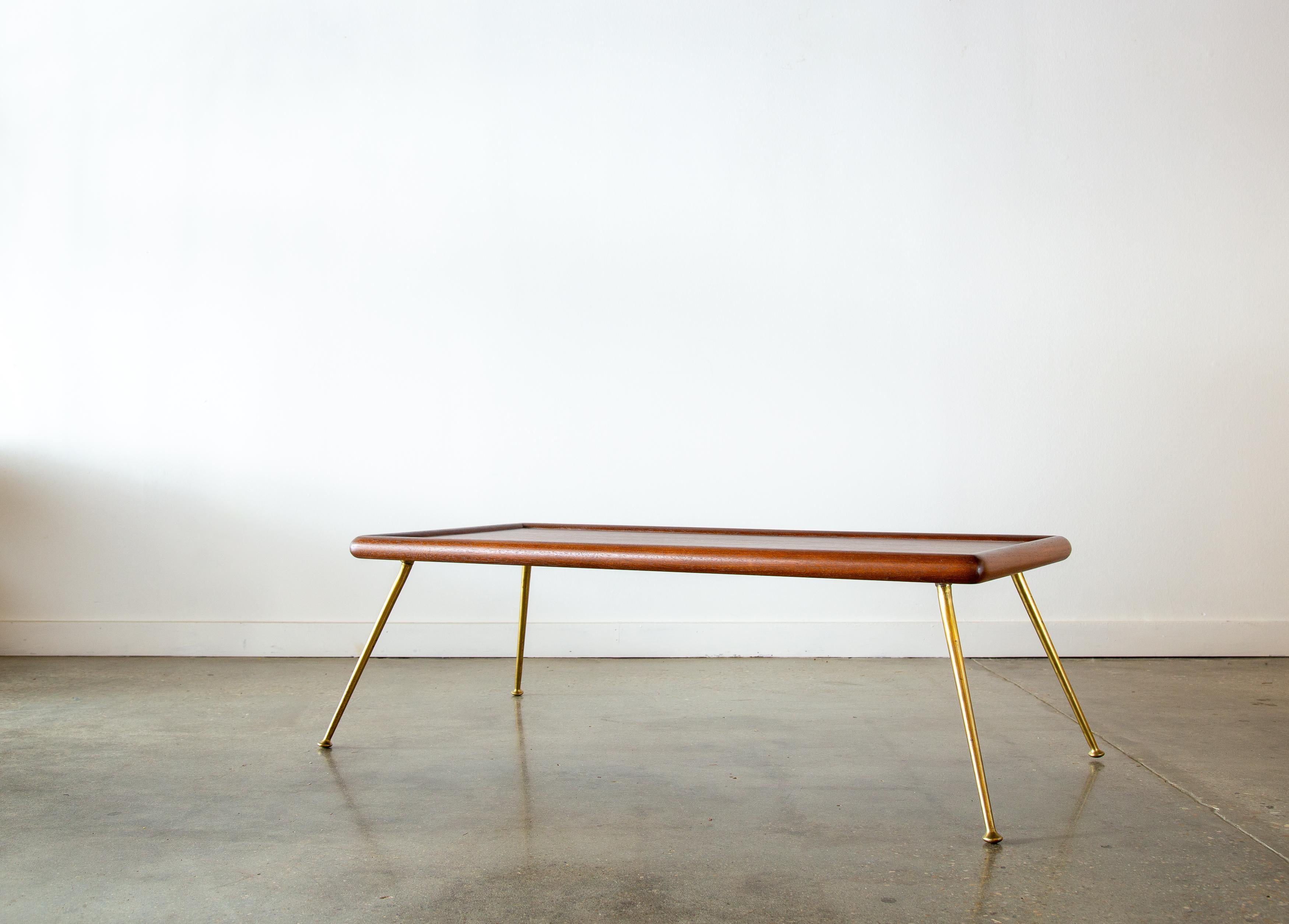 An iconic T.H. Robsjohn Gibbings for Widdicomb brass leg coffee table or bench.  A slab of mahogany floats on splayed brass legs. Exaggerated bull nose edge, with a raised lip around the circumference.  This table with distinct New York vibe works