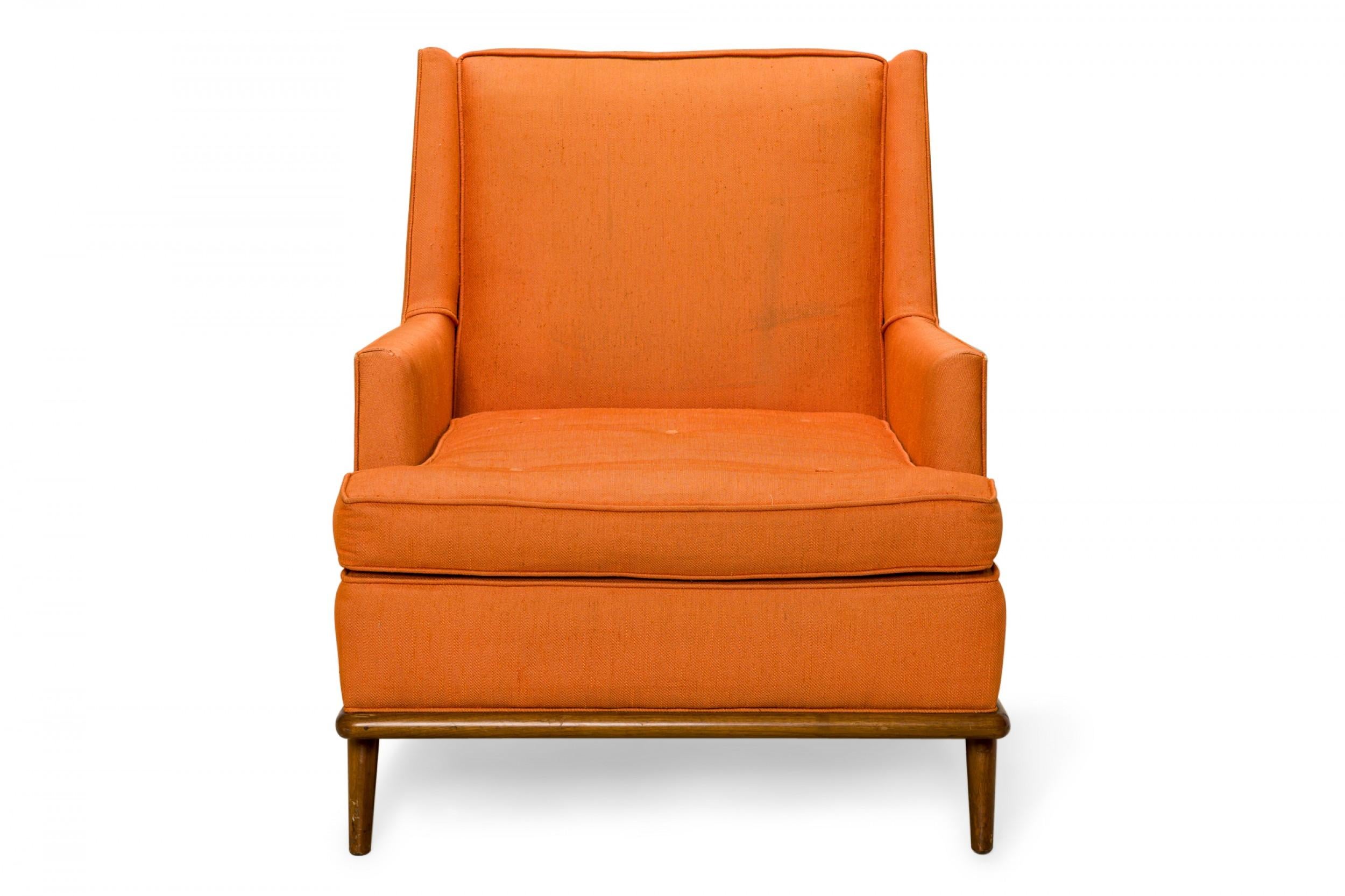 American mid-century lounge armchair with a high back and bright orange fabric upholstery, resting on a walnut base with four short tapered dowel legs. (T.H. ROBSJOHN-GIBBINGS FOR WIDDICOMB)
 