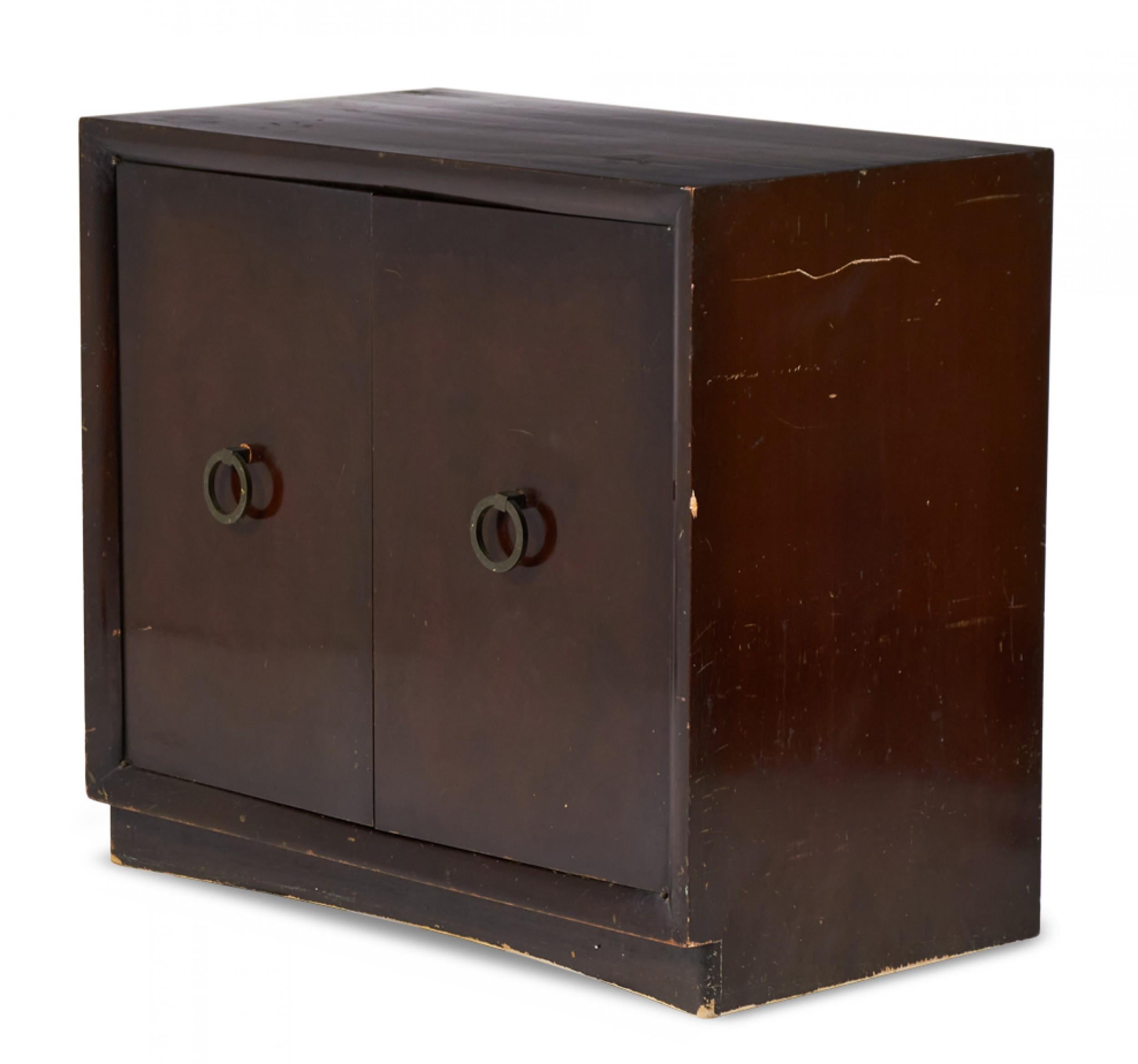 American Mid-Century (1950s) two-door mahogany cabinet with brass ring-shaped door pulls, resting on four small concealed casters. (T.H. ROBSJOHN-GIBBINGS FOR WIDDICOMB MODERN).
 
