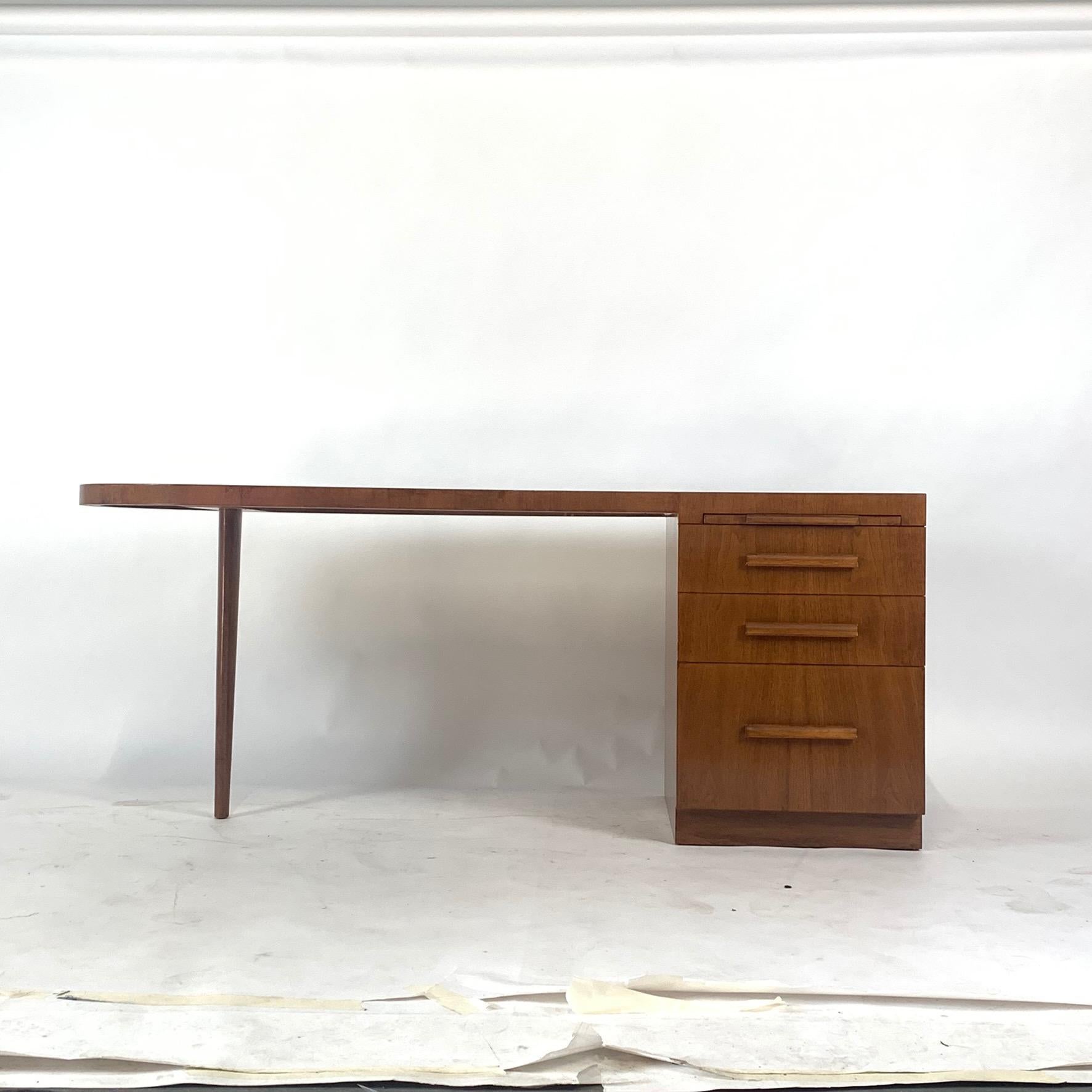 A modern executive desk, created by designer T.H. Robsjohn-Gibbings for Widdicomb circa 1950s, comes in birch and features three graduated drawers and pull-out writing surface, supporting a curved streamlined top on opposite single tapered leg. The
