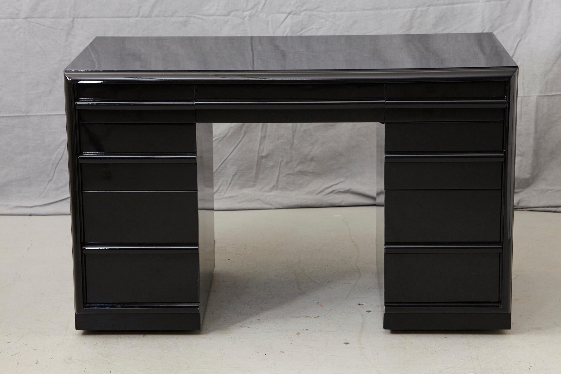 Stunning T.H. Robsjohn-Gibbings kneehole or double pedestal desk in new black piano lacquer finish.
The desk is equipped with 3 drawers in each pedestal and a middle drawer mounted on casters.
The kneehole measurements are as follows: W 20.25