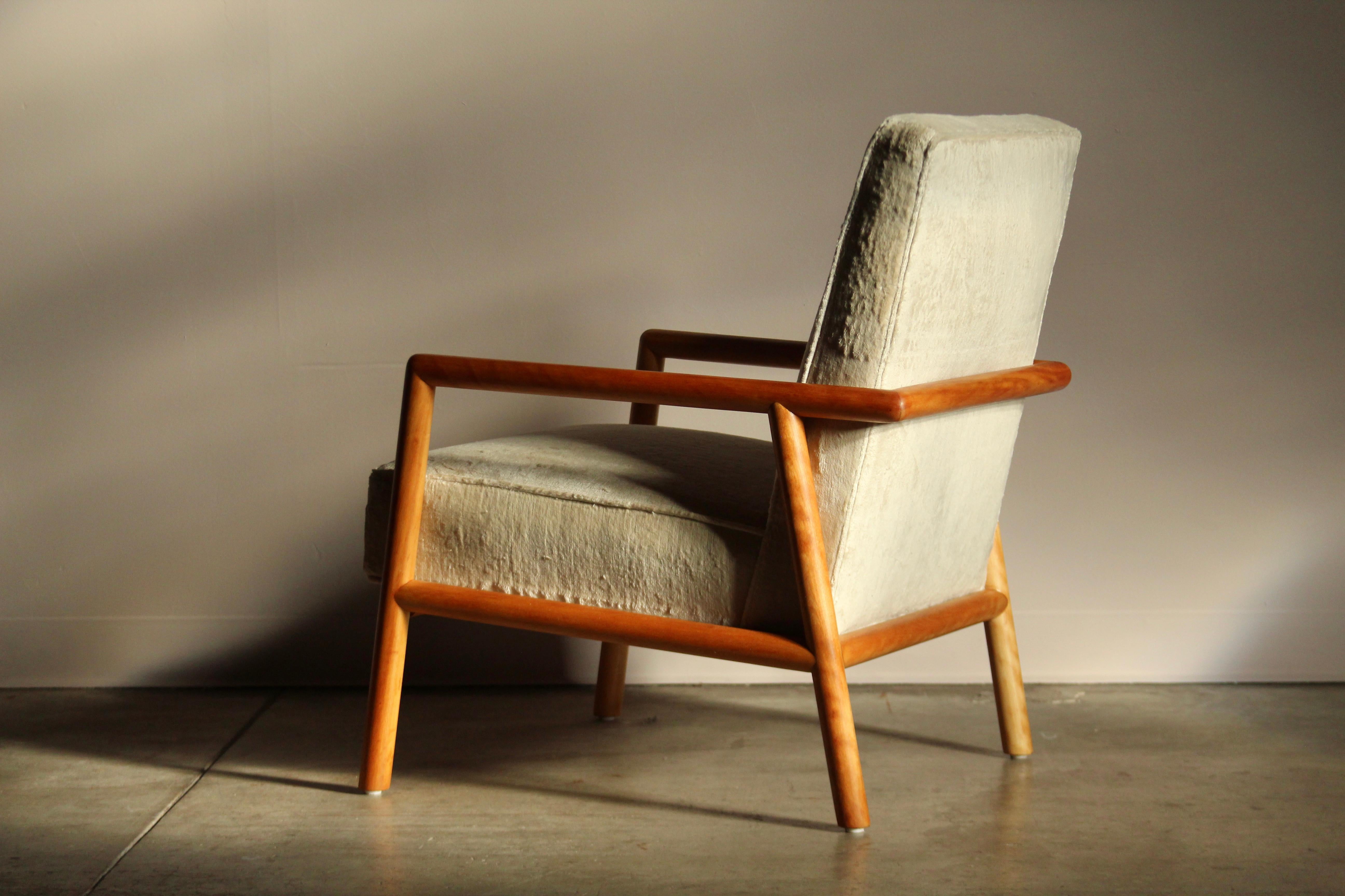 A stunning lounge chair designed by T.H. Robsjohn-Gibbings and produced by Widdicomb in the mid 1950s in Grand Rapids, Michigan. This uncommon chair features a beautifully sculpted frame of blonde stained walnut, and a thick seat and back cushion