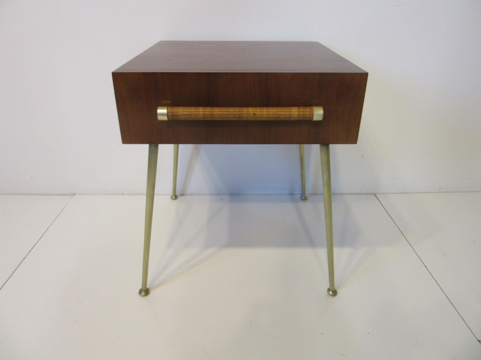 A beautifully crafted and fine quality side table / nightstand in a rich dark walnut with raffia wrapped handle and brass details to one single drawer sitting on long sexy brass legs. Retains the original fabric label in the drawer manufactured by