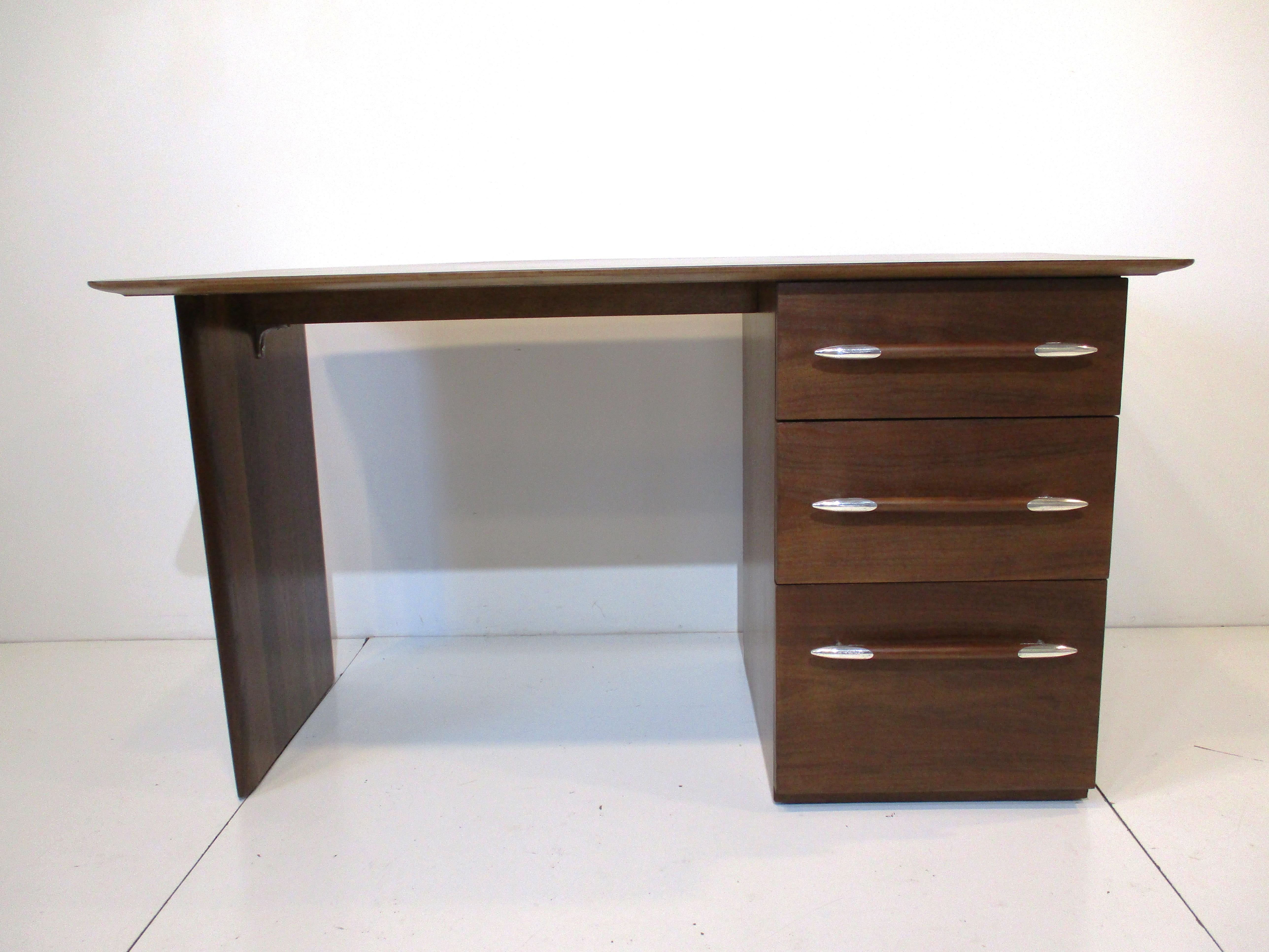 A rare nicely crafted and scaled dark mahogany desk with three drawers having silverplated spear handle tips, the top drawer having pen and paperclip holder. The second drawer has slip in paperwork holder and the bottom has a full file drawer. The