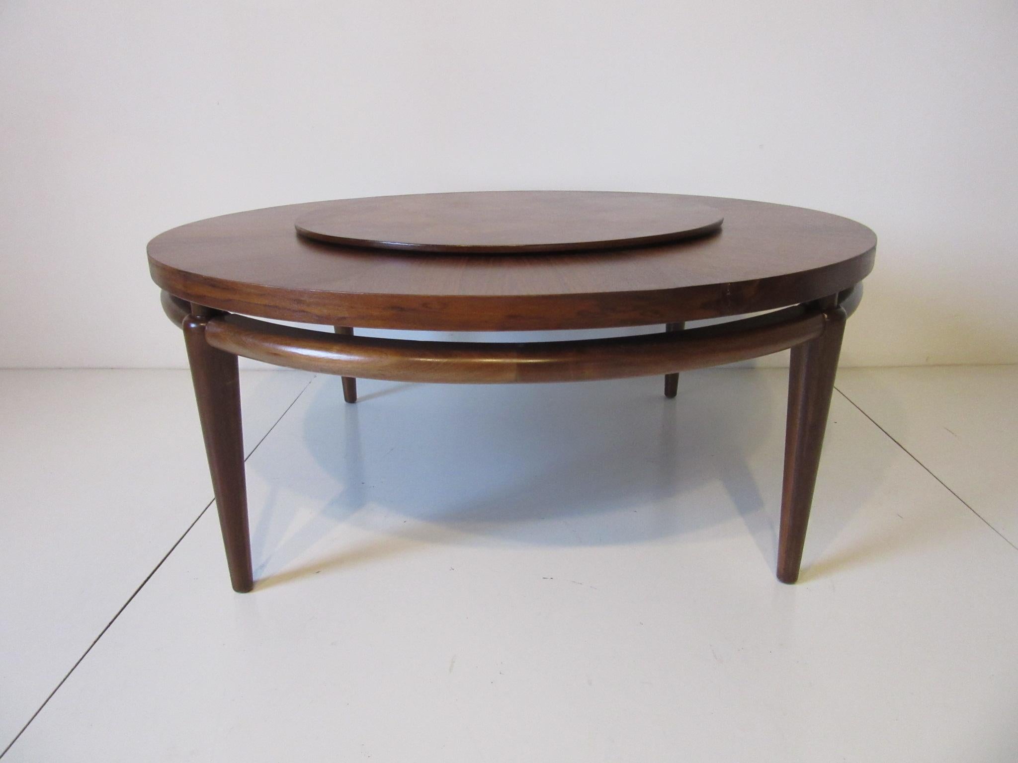 A well crafted walnut coffee table with bookmatched outer area and burl wood Lazy Susan styled center section. Below the top is a rounded stretcher and conical legs designed in the manner of T.H. Robsjohn - Gibbings. The tabletop measurement is 42
