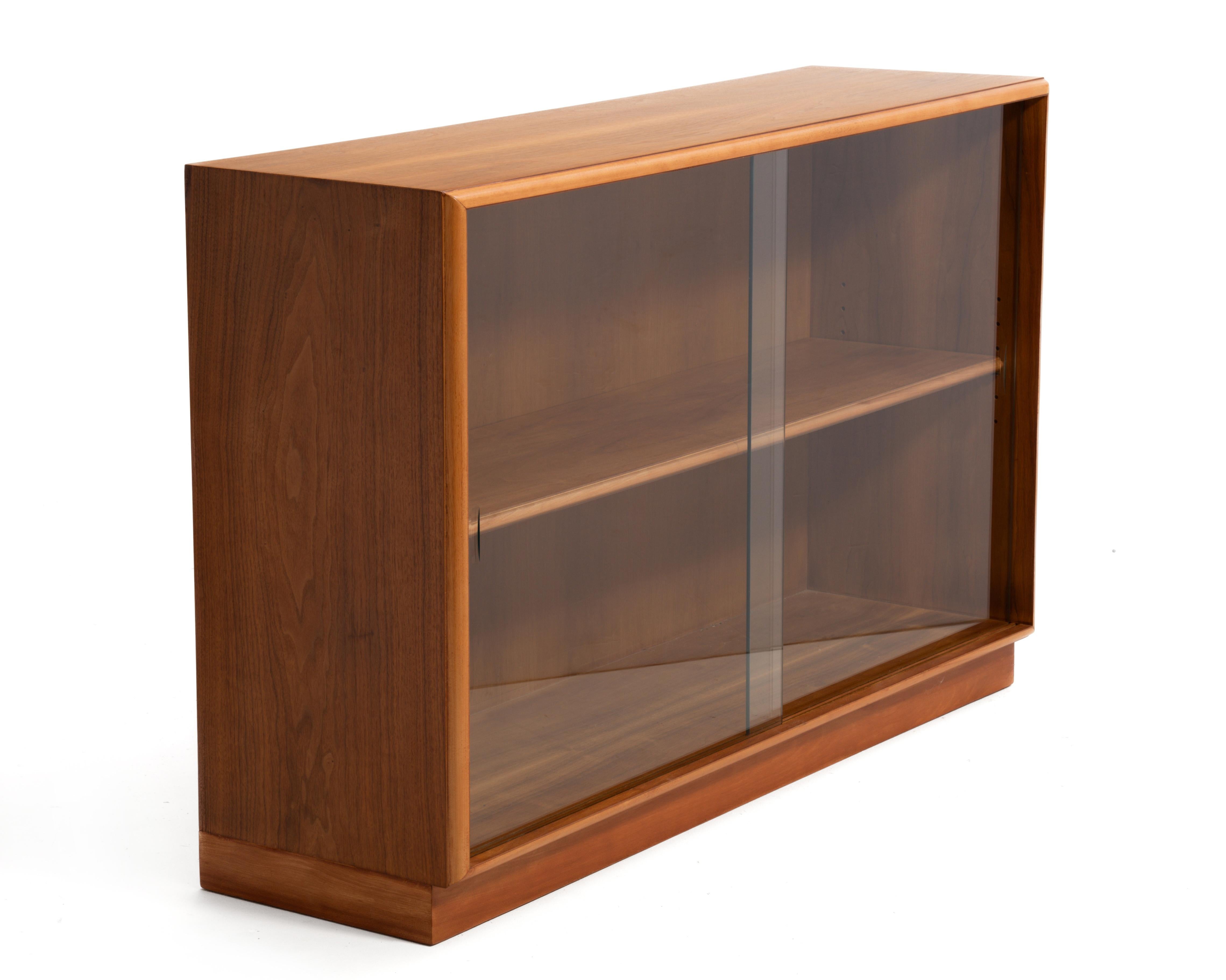 A Mid Century walnut bookcase with sliding glass doors designed by T.H. Robsjohn Gibbings for Widdicomb. Fully marked on the bottom and produced in September of 1951.
