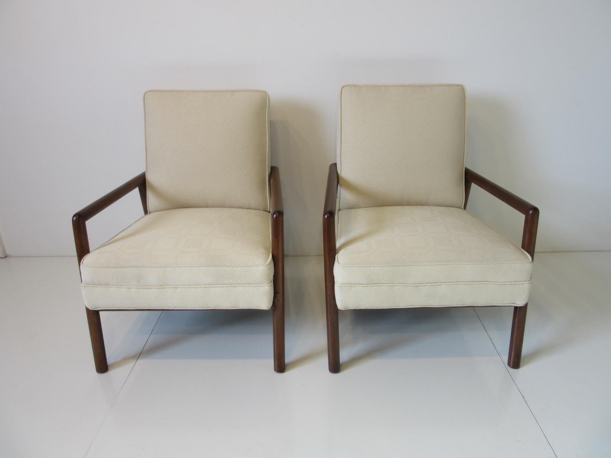 A pair of upholstered lounge chairs in a cream toned patterned fabric with walnut finished frames a very comfortable and stylish lounger manufactured by the Widdicomb furniture company.