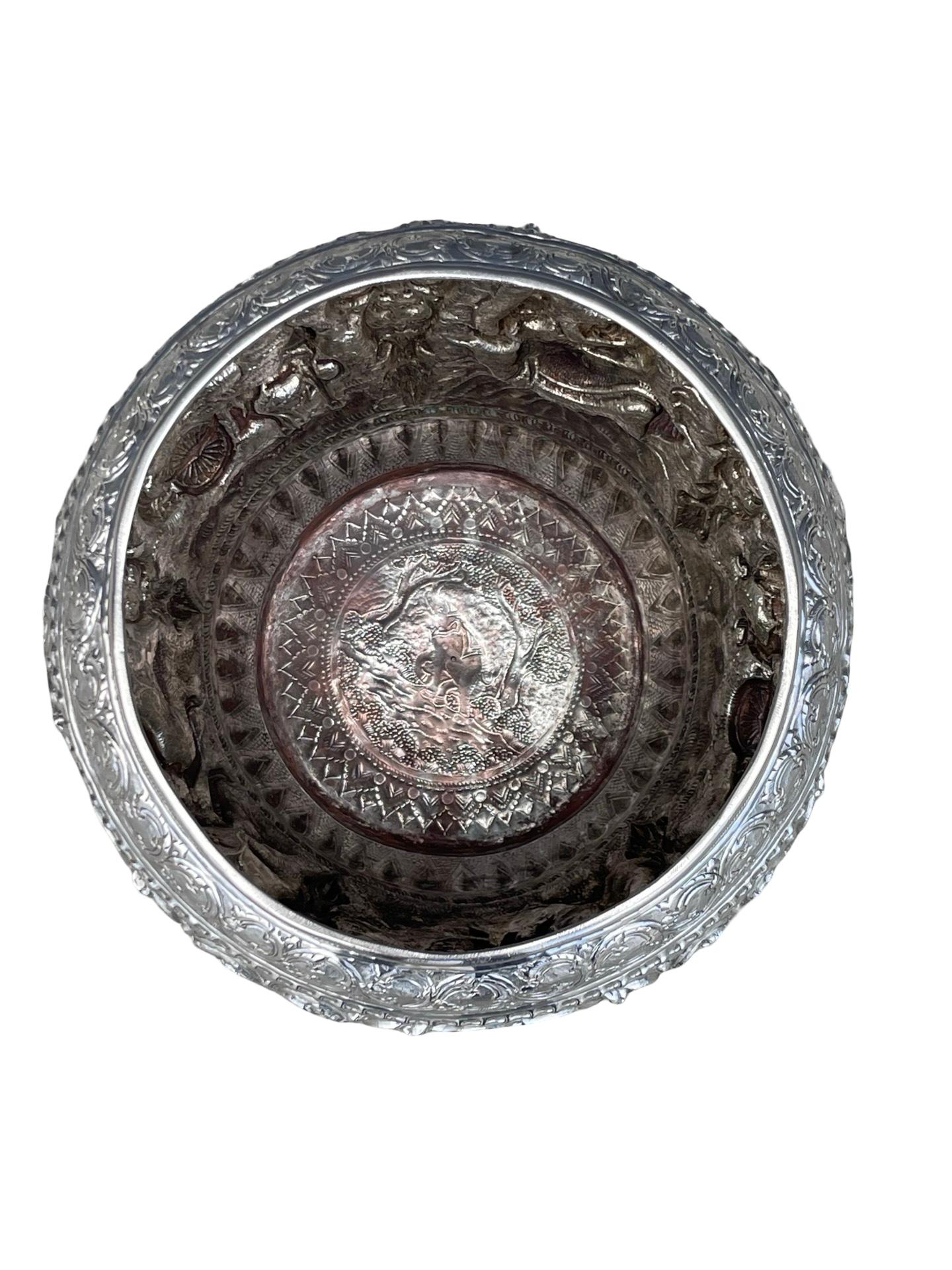 Of vase form, the body richly embossed and chiseled with traditional scenes from Burmese mythology and adorned with numerous decorations.