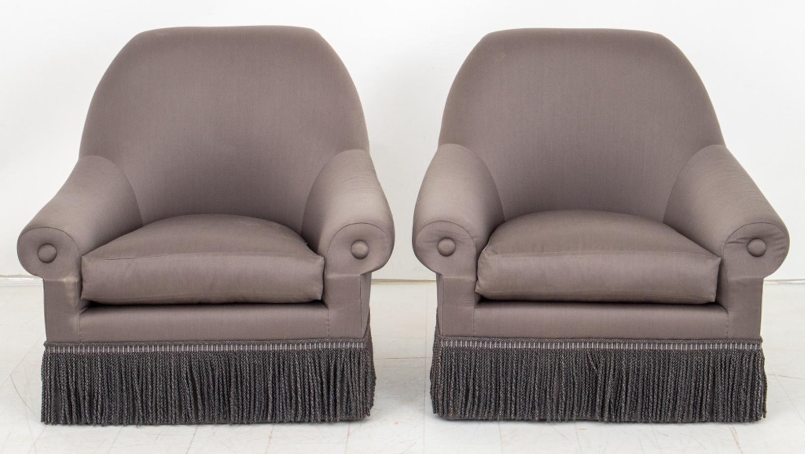 Thad Hayes (American, XX-XXI) designed swivel arm chairs or bergères, upholstered allover in graphite-colored silk, the scrolling back and rounded arms with button details, above a seat rail with coordinating Bullion fringe above swivel base.