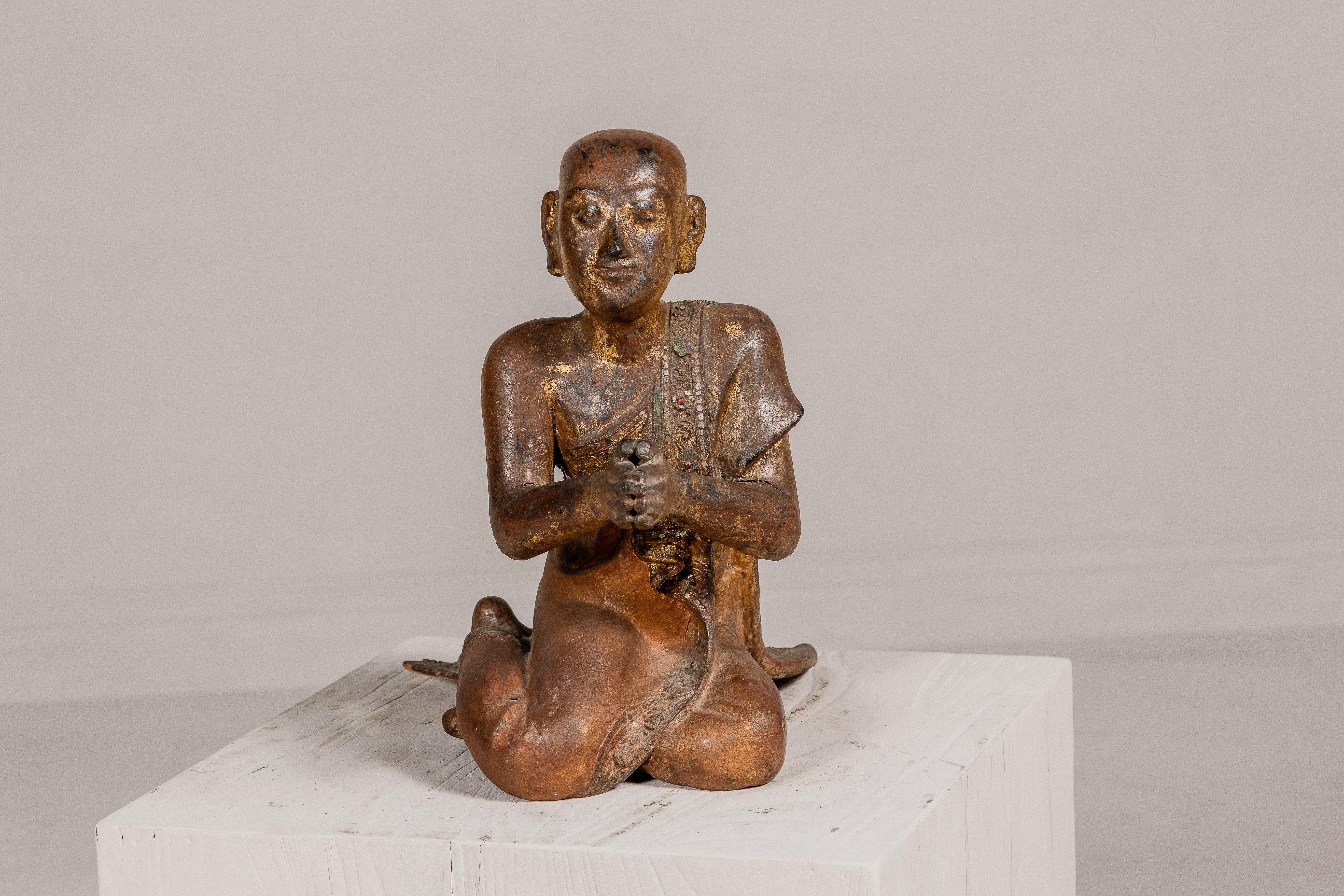 A Thai religious hand carved wooden statue of a seated Buddhist monk with polychrome and gilded accents from the early 20th century. This early 20th-century Thai statue, masterfully hand-carved, captures the tranquil essence of a seated Buddhist