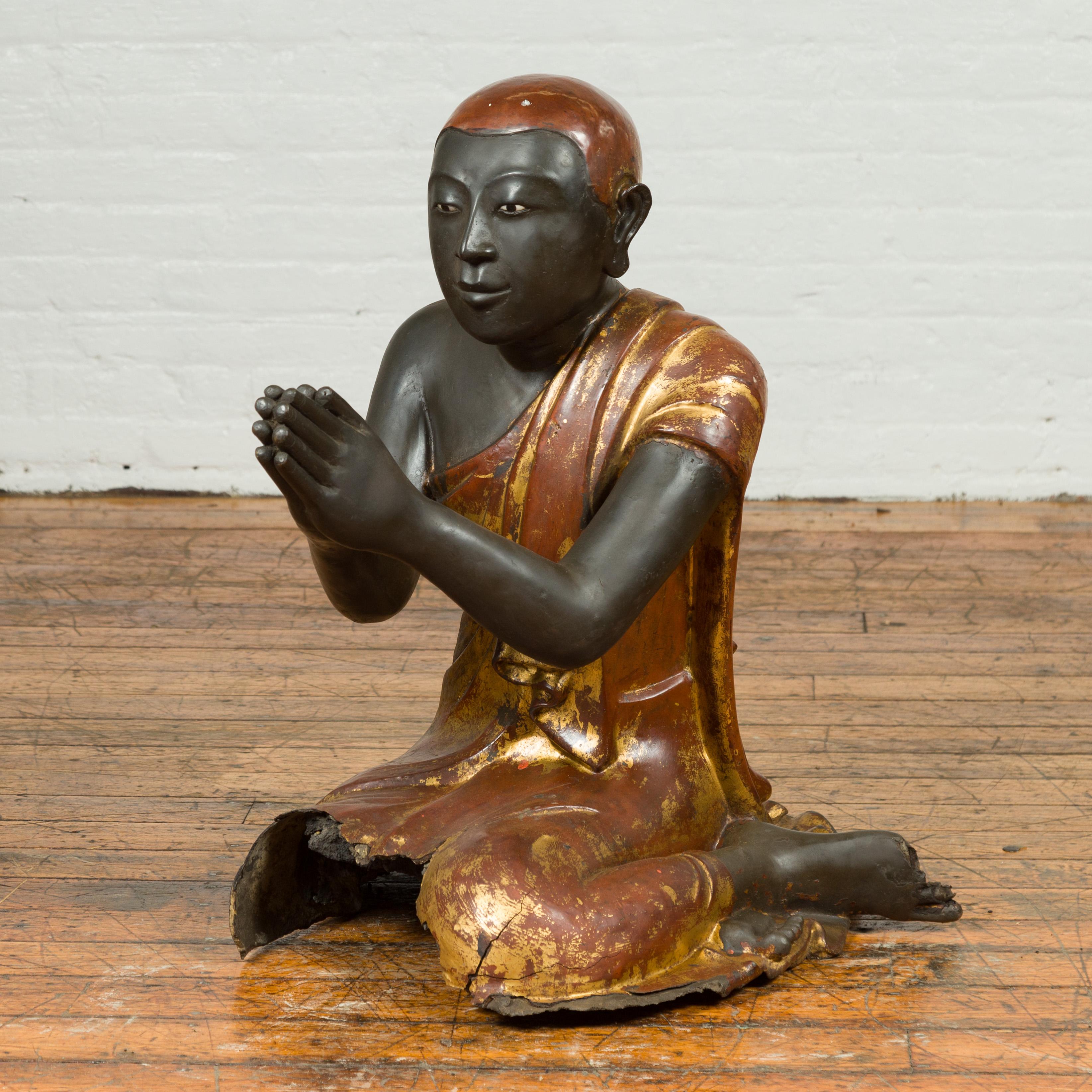 A Thai kneeling ceremonial monk sculpture from the 20th century with hand painted gilt and lacquer over stone. This 20th-century Thai kneeling ceremonial monk sculpture, sourced from a temple, is an authentic piece of Southeast Asian art. With its