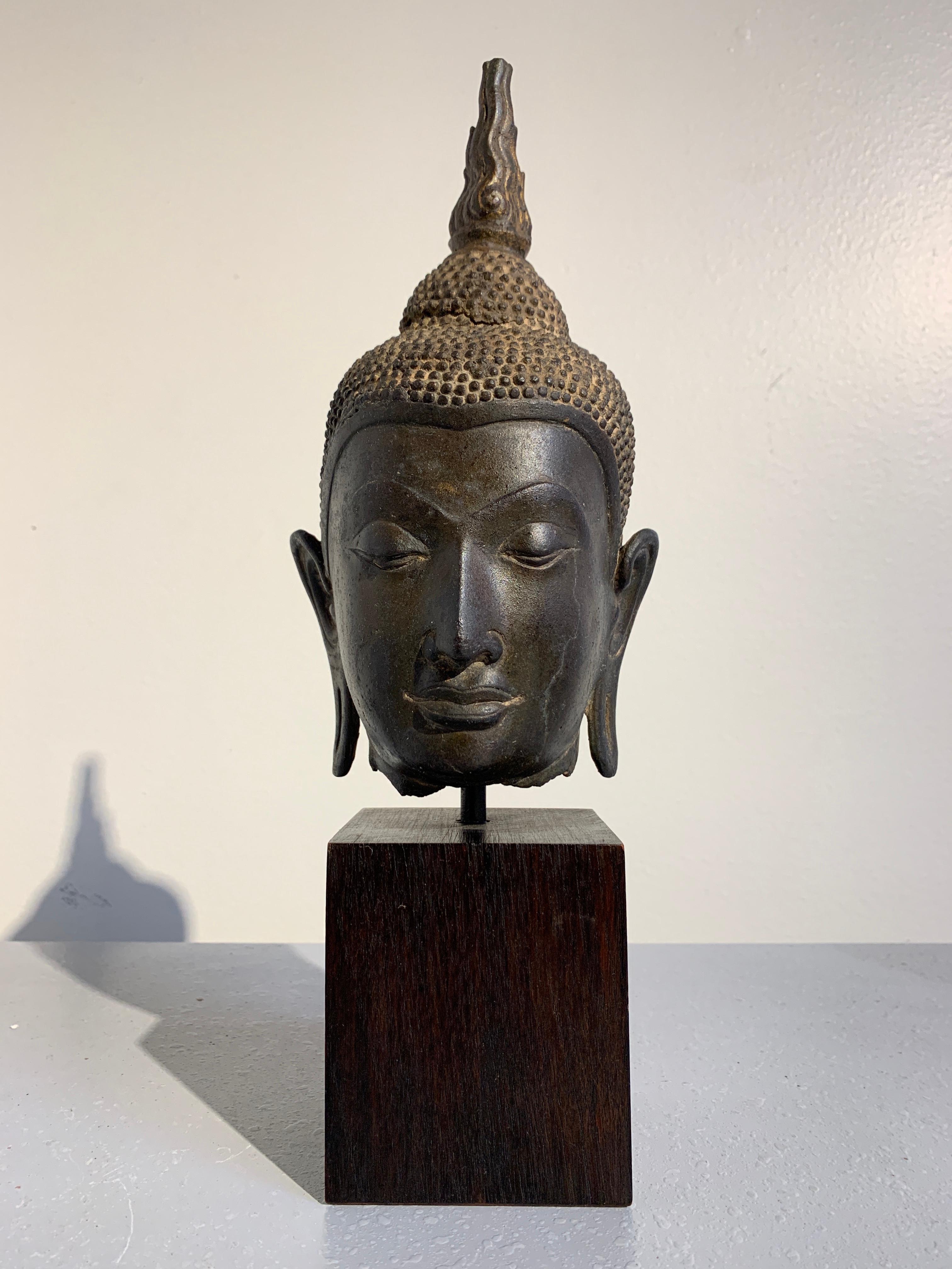 Tête de Bouddha en bronze thaïlandais:: fine et expressive:: provenant du Royaume d'Ayutthaya:: Thaïlande:: 14e-15e siècle. 
La tête de Bouddha est délicatement moulée avec des traits de visage naturalistes centrés sur un nez patricien. Le Bouddha