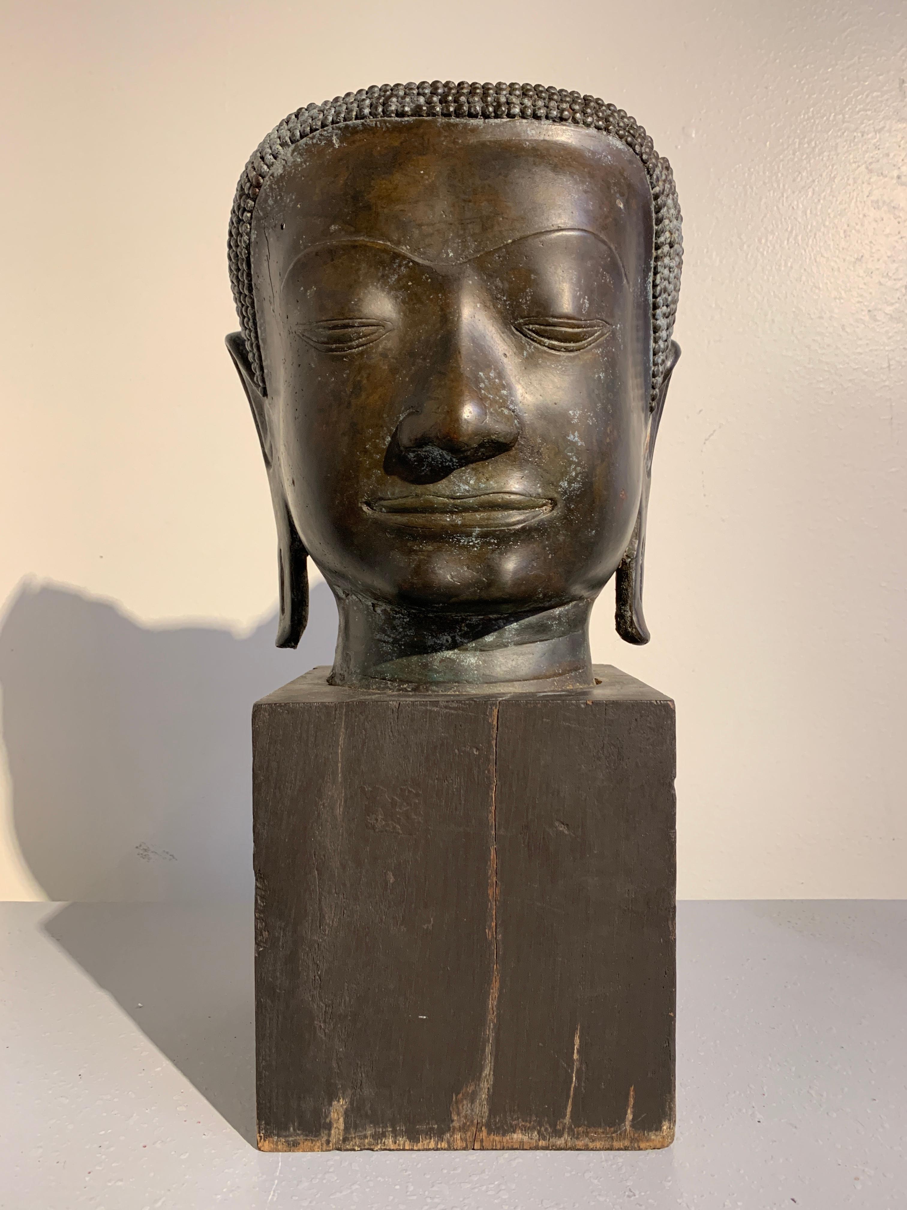 A sublime Thai Ayutthaya Period U-Thong A style life-sized bronze head of the Buddha, circa 14th-15th century.
The beautiful and serene face of the Buddha, framed by a narrow band under neatly arranged coiled hair and long, pendulous earlobes,