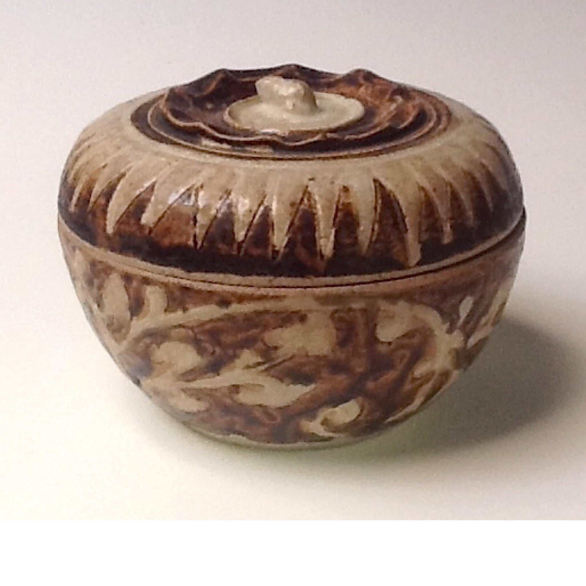 Thai ceramic covered box from the Sawankhalok kilns of globular fruit form with pinched foliate rim and sepal stem finial on top decorated in brown and white glaze in a peaked zigzag design at the the shoulder and foliate scroll pattern on the body,