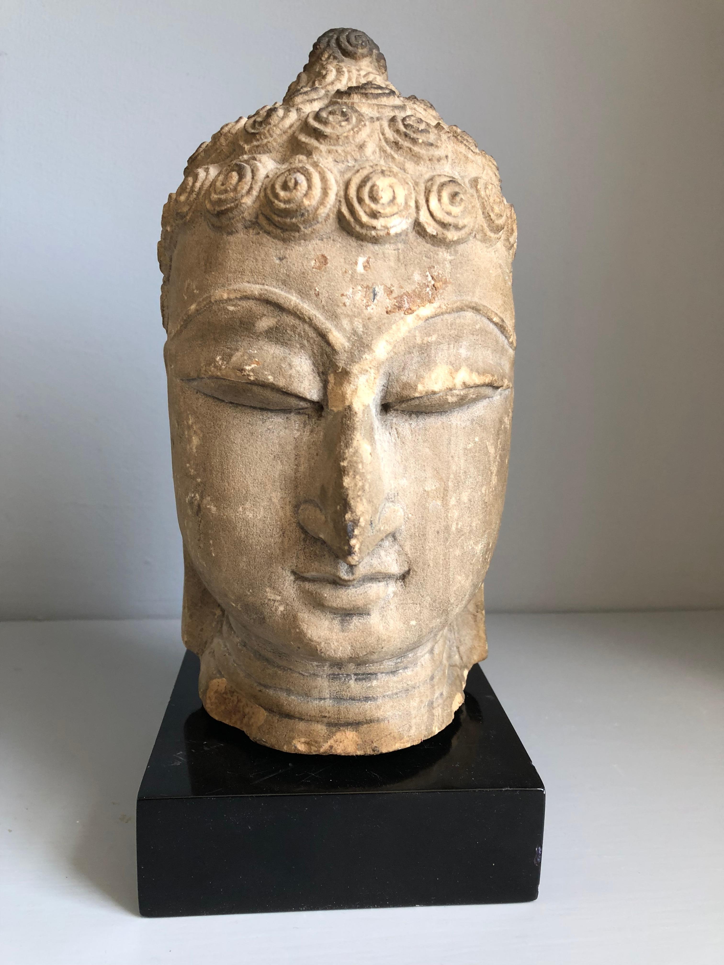 A Thai Buddha head sculpture in sandstone, Ayutthaya period, 18th century or earlier, finely sculpted, depicting the Buddha in a serene meditating pose, with a custom black lacquer base (not attached).
Head measures 5” diameter x 9” high.