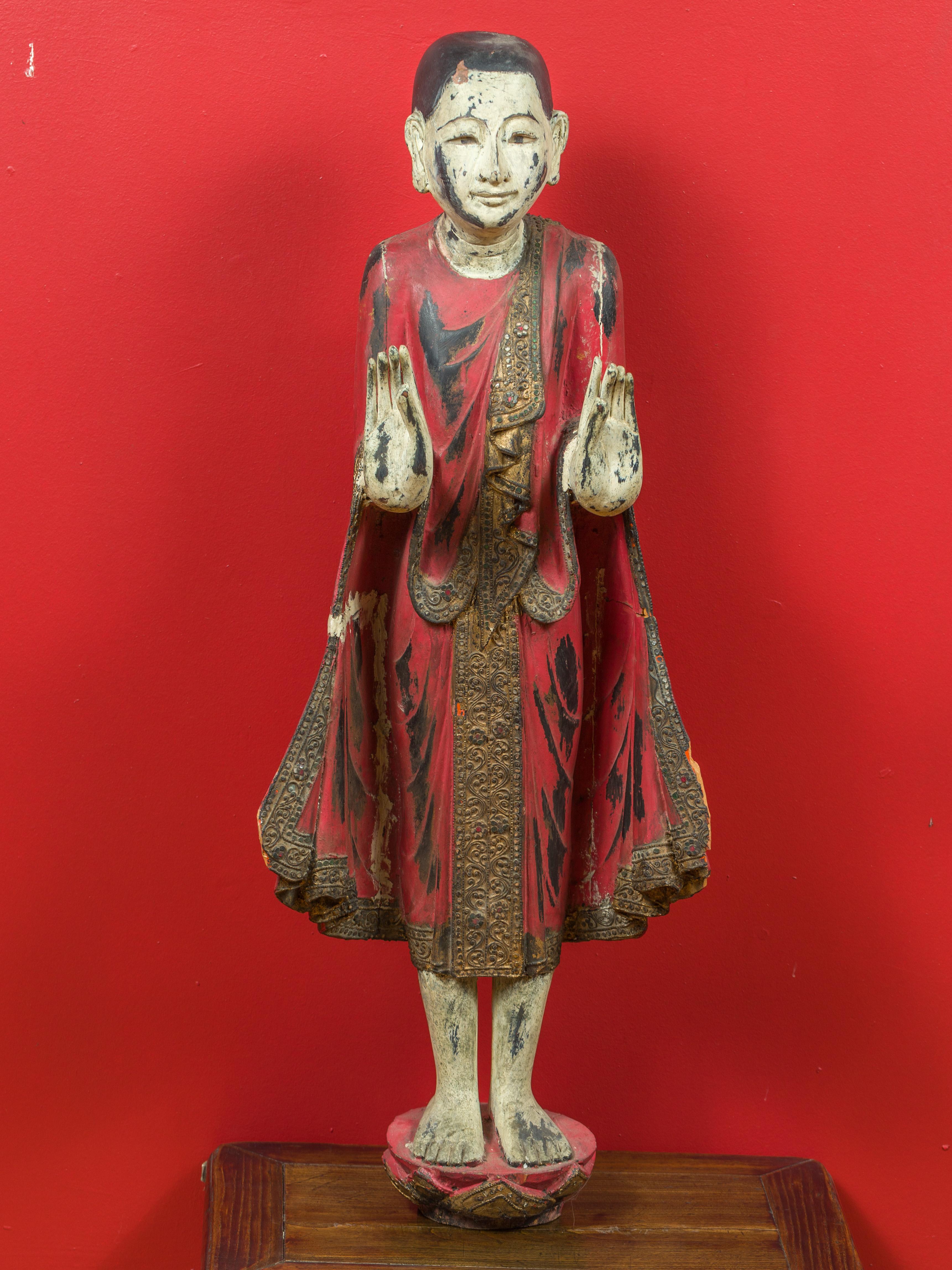 A vintage Thai carved wooden monk statue with red, black and gilt finish, inlaid mica and Abhaya Mudra (fear dispelling) gesture. Immerse yourself in the serene beauty of this vintage Thai carved wooden monk statue, a remarkable piece from Thailand.