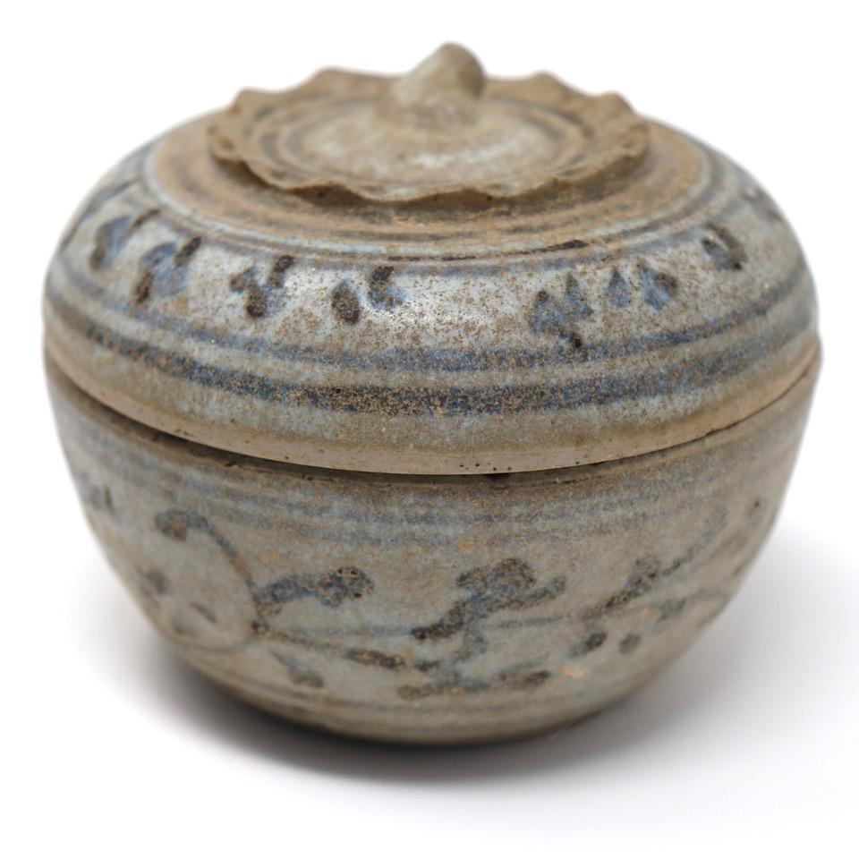 Caja de cerámica tailandesa con tapa, procedente de los hornos de Sawankhalok, de forma globular de caqui con borde foliado pinzado y remate de tallo de sépalo en la parte superior decorado en marrón hierro/negro  glaseado en  bandas dobles que