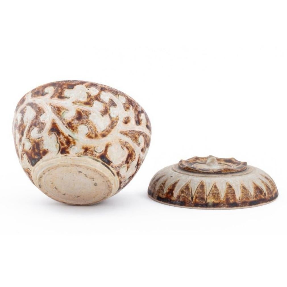 Thai ceramic covered box from the Sawankhalok kilns. Globular fruit form with pinched foliate rim and sepal stem finial on top decorated in brown and white glaze in a peaked zigzag design at the the shoulder and a white foliate scroll pattern on a