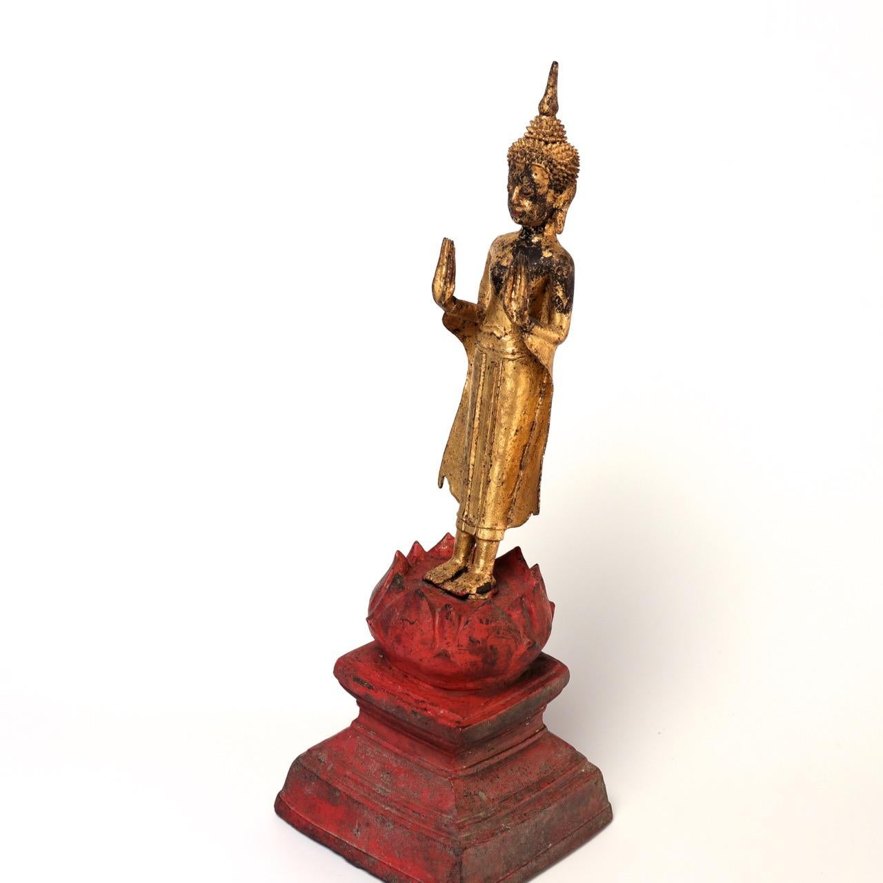 Thai Gilt Bronze figure of a Standing Buddha Image, upright with both hands extended forward and slightly up from the elbow, wrists bent backward, palms face forward with the long elegant tapering fingers reaching towards the heavens, exaggerating