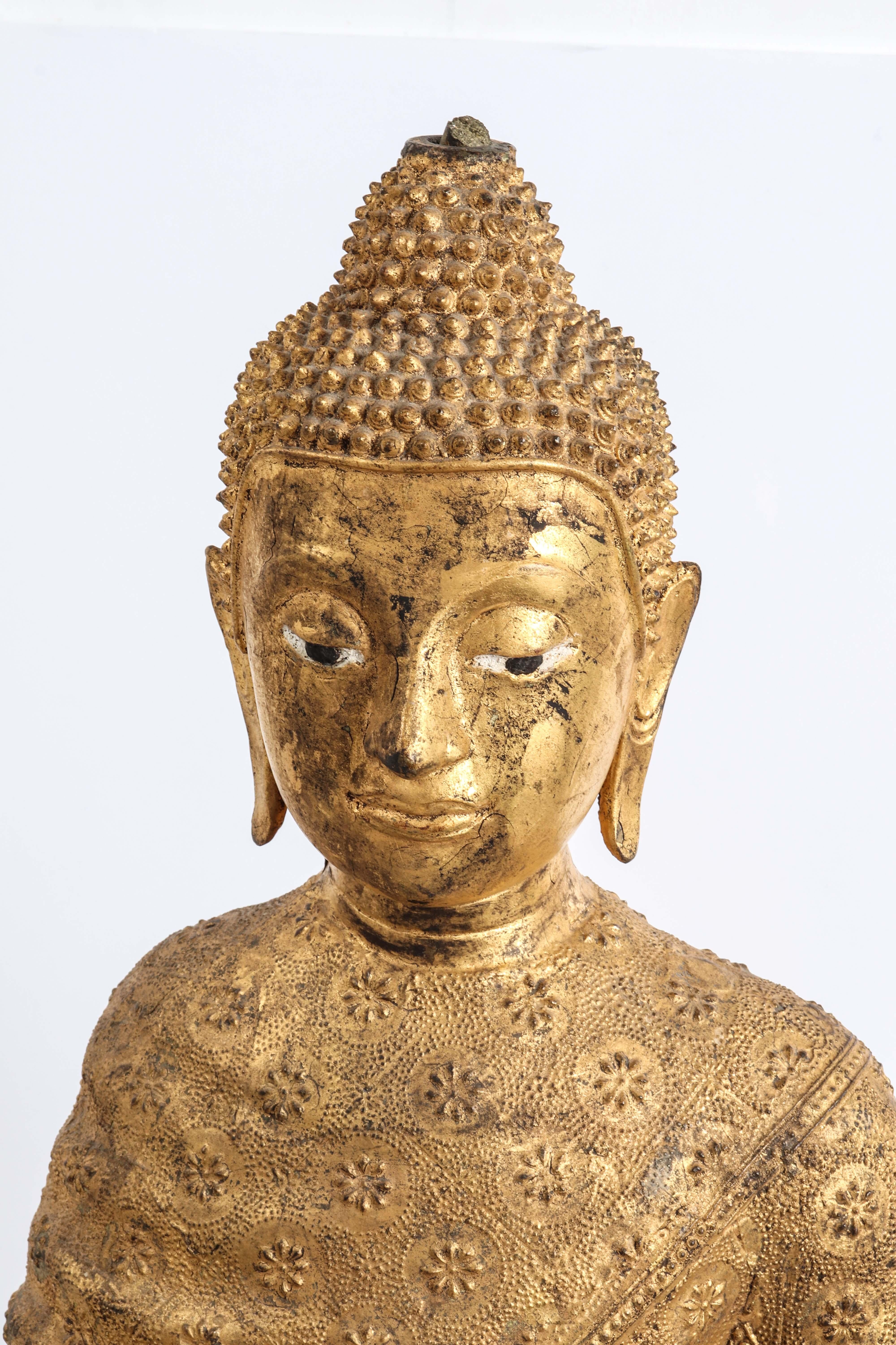Thai gilt bronze sculpture of a standing Buddha in Abhaya mudra. The piece presents characteristics of the Rattanakosin period and dates from the 19th century/early 20th century. The figure is cloaked in a robe with all-over relief floral pattern