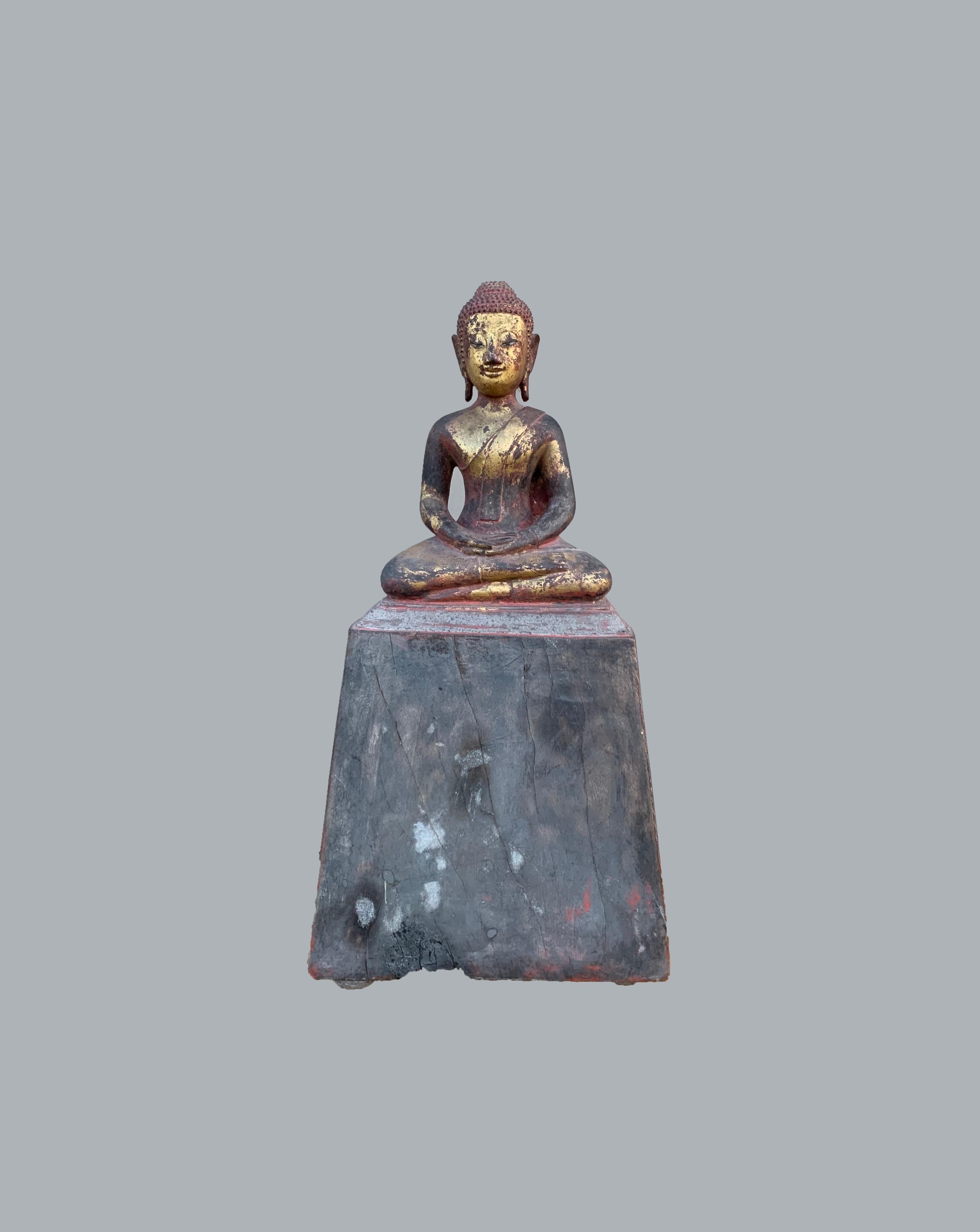This buddha is a hand-carved from wood and once occupied a temple shrine in Northern Thailand. It has been lacquered in black and red and then gilded (covered with gold leaf). There are clear burn marks on its frontal side from having occupied a