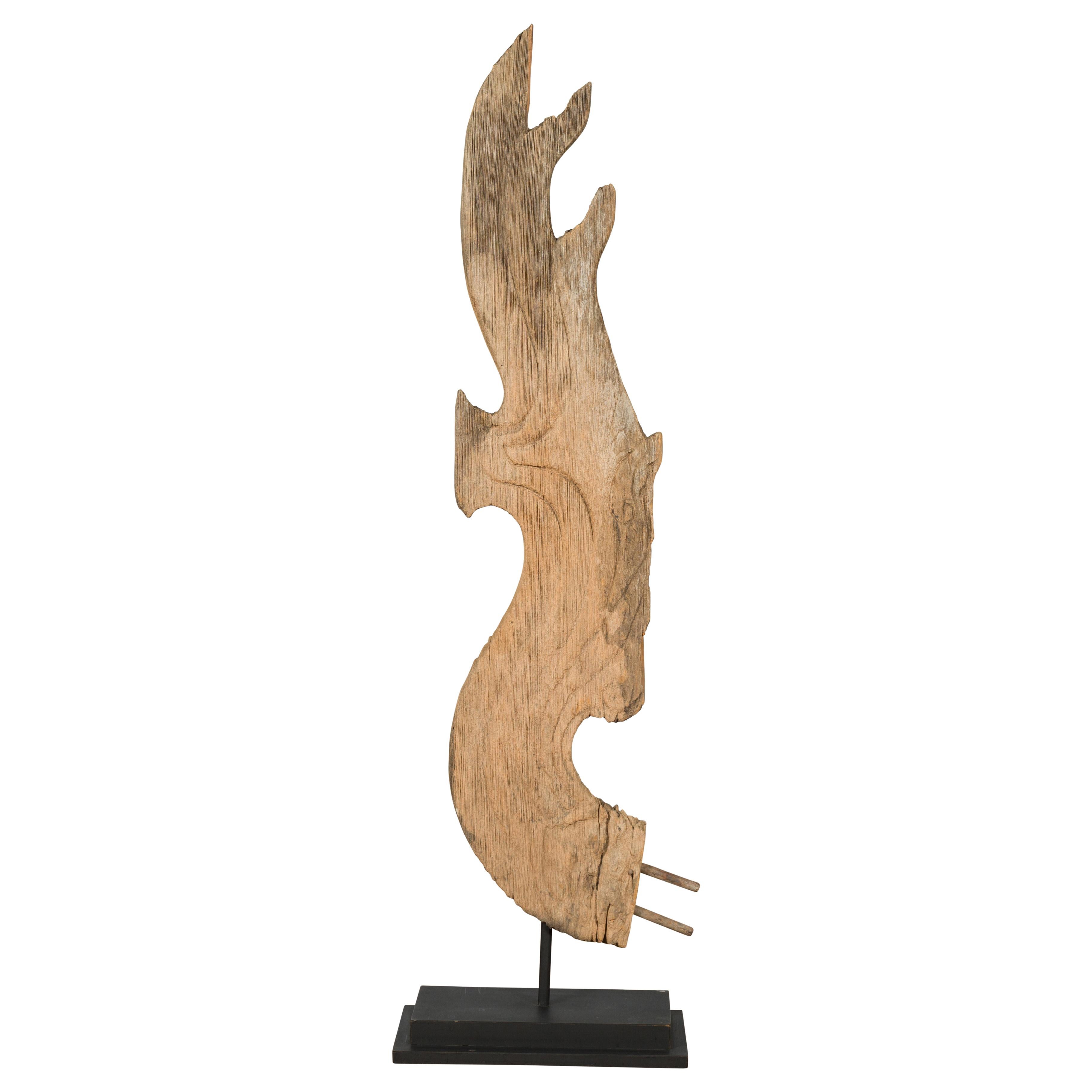 A Thai carved wooden temple dragon sculpture from the 19th century, mounted on a custom base. Created in Thailand, this abstracted wooden dragon sculpture adopts a curved shape evoking both wings and flames. The front features subtle incised lines
